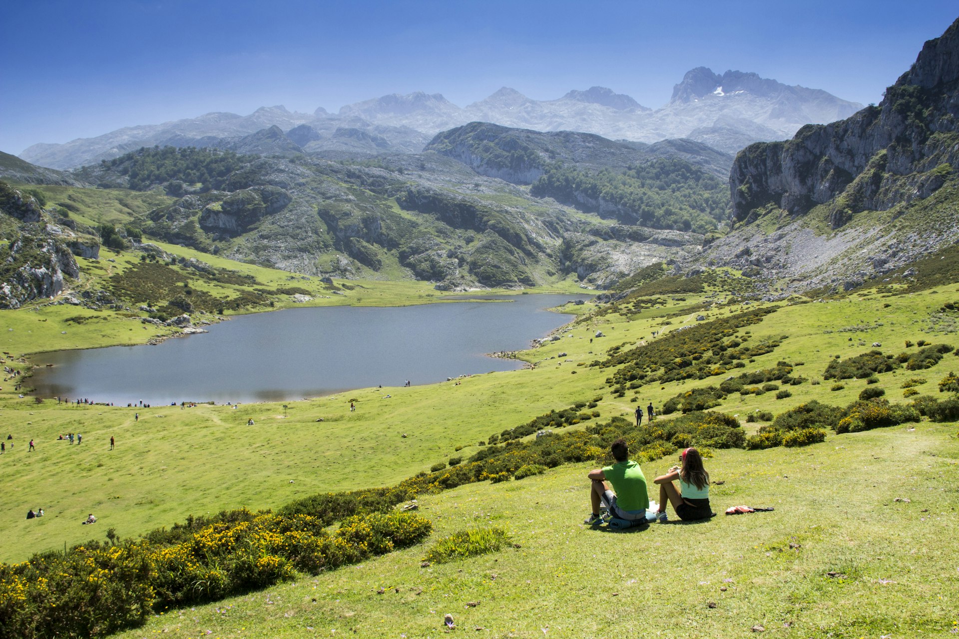 Jovem casal sentado na grama com vista para os lagos em uma região montanhosa