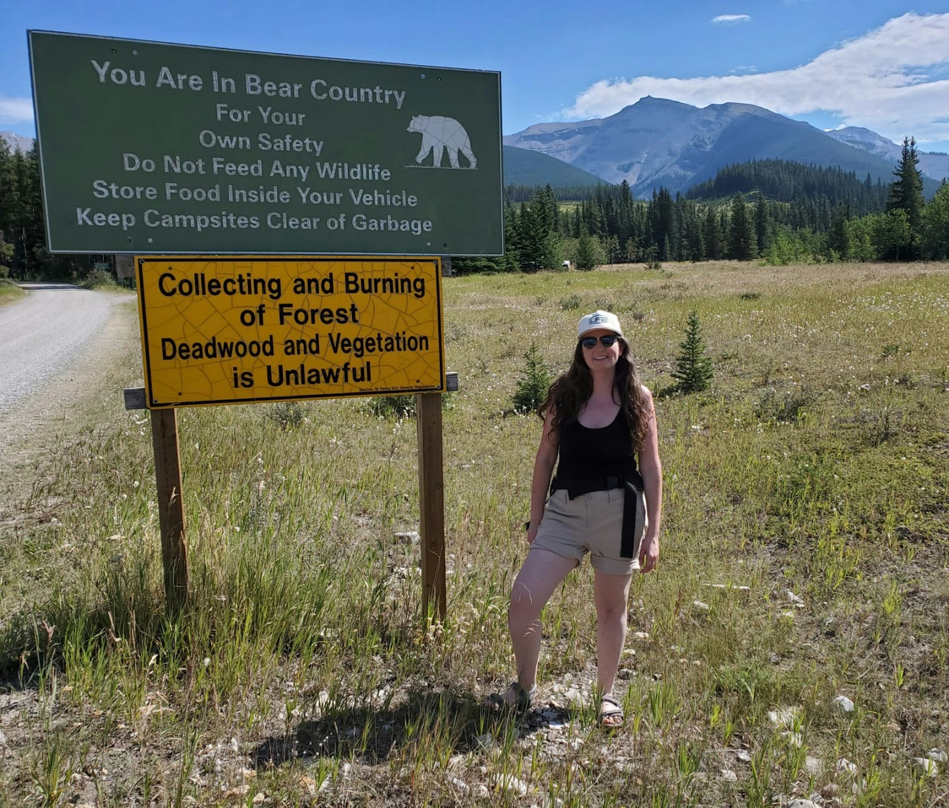 A woman stands by a sign stating that she is in Bear Country and must not feed any wildlife