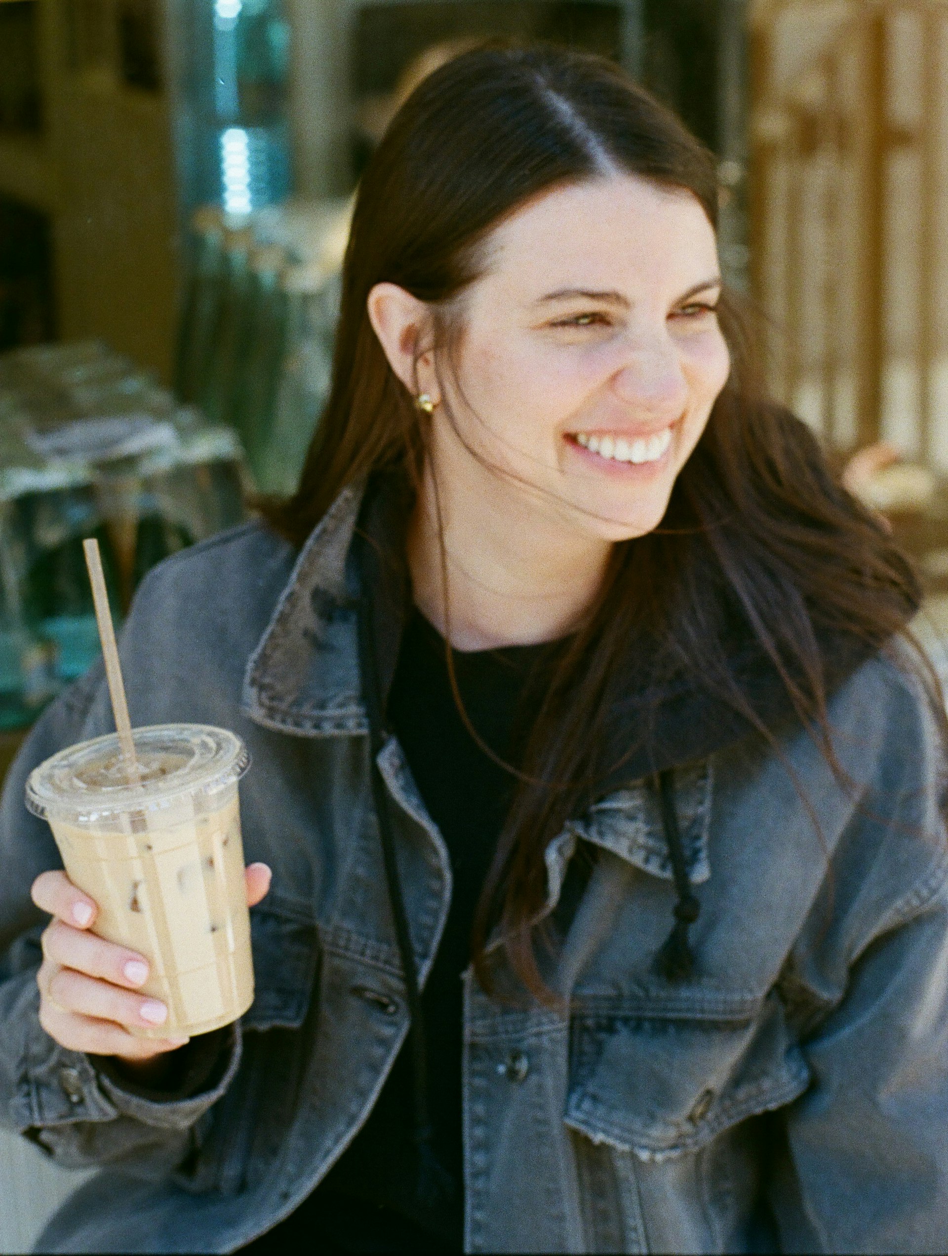 A woman sitting outside a coffee shop smiling and holding a latte