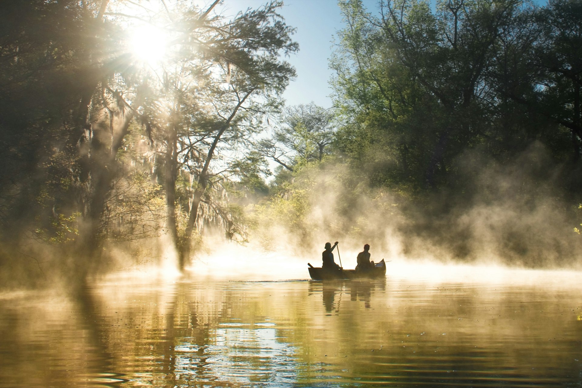 People paddle in kayaks in the Everglades, as mist rises around them
