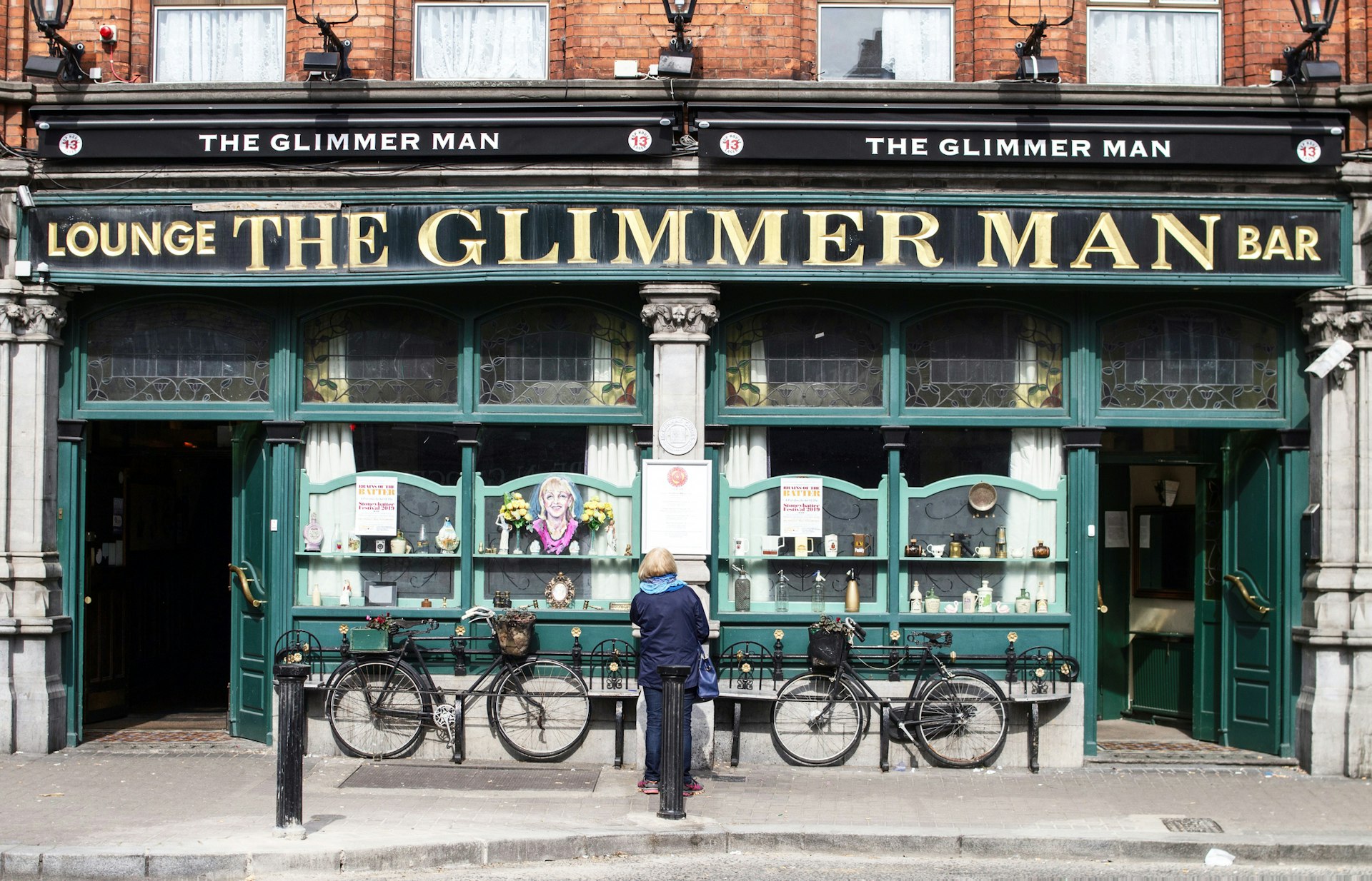 A woman stands facing the facade of an old pub called The Glimmer Man