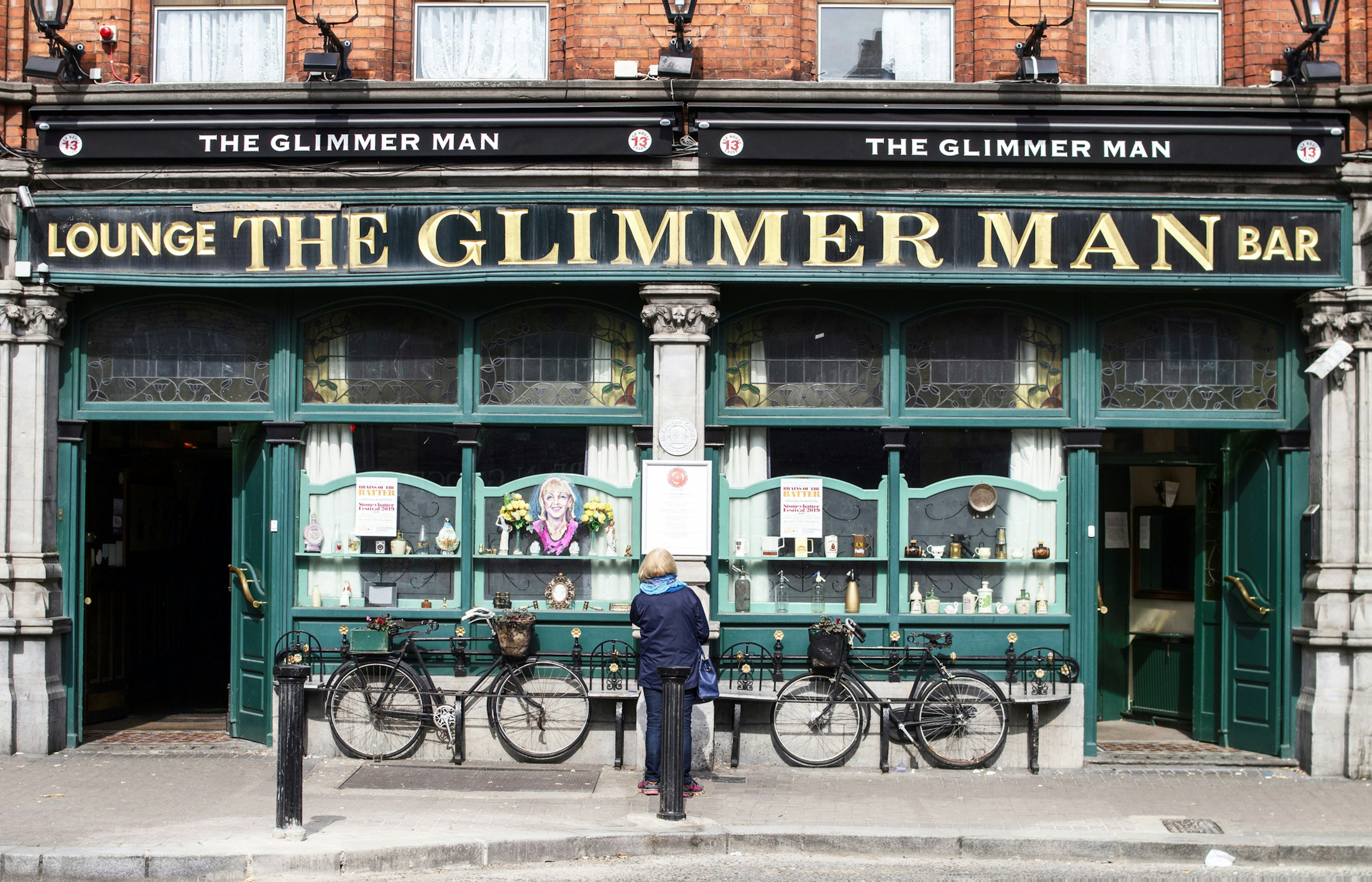 A woman stands facing the facade of an old pub called The Glimmer Man