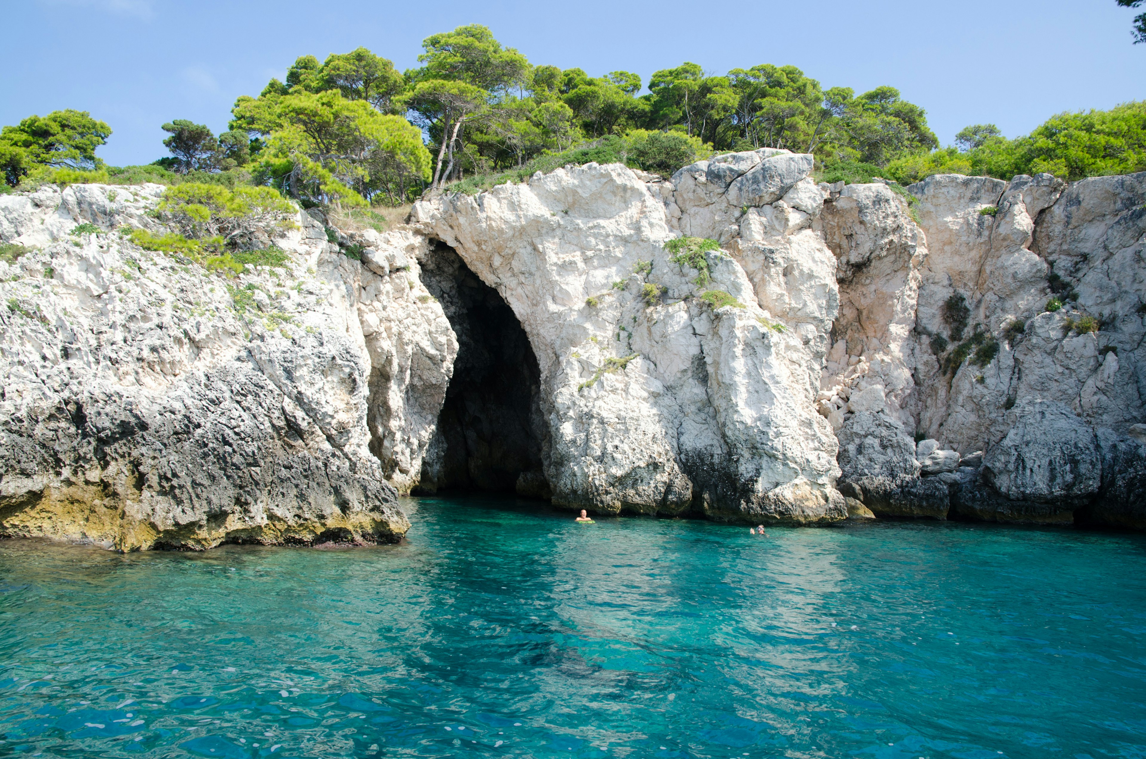 A person floats above the surface of the sea near an opening to a cave