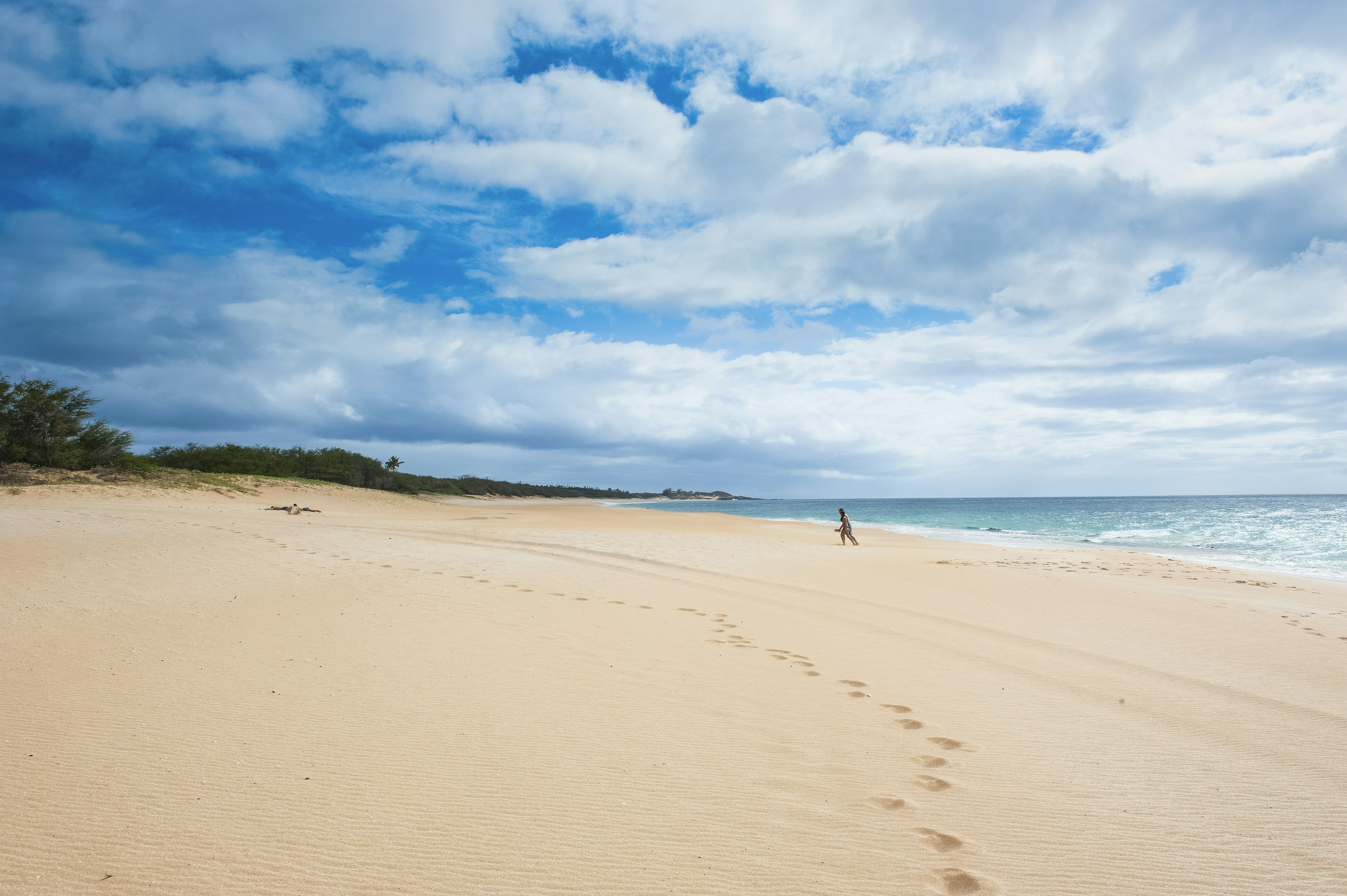 A single distant figure on a large sandy beach that's completely empty of people