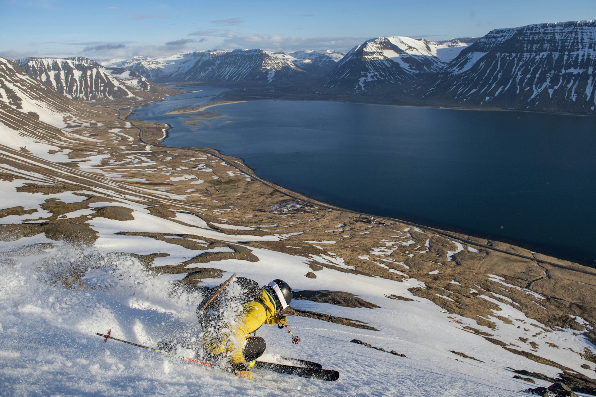 A skier glides along a snow-covered mountainous landscape just above a lake