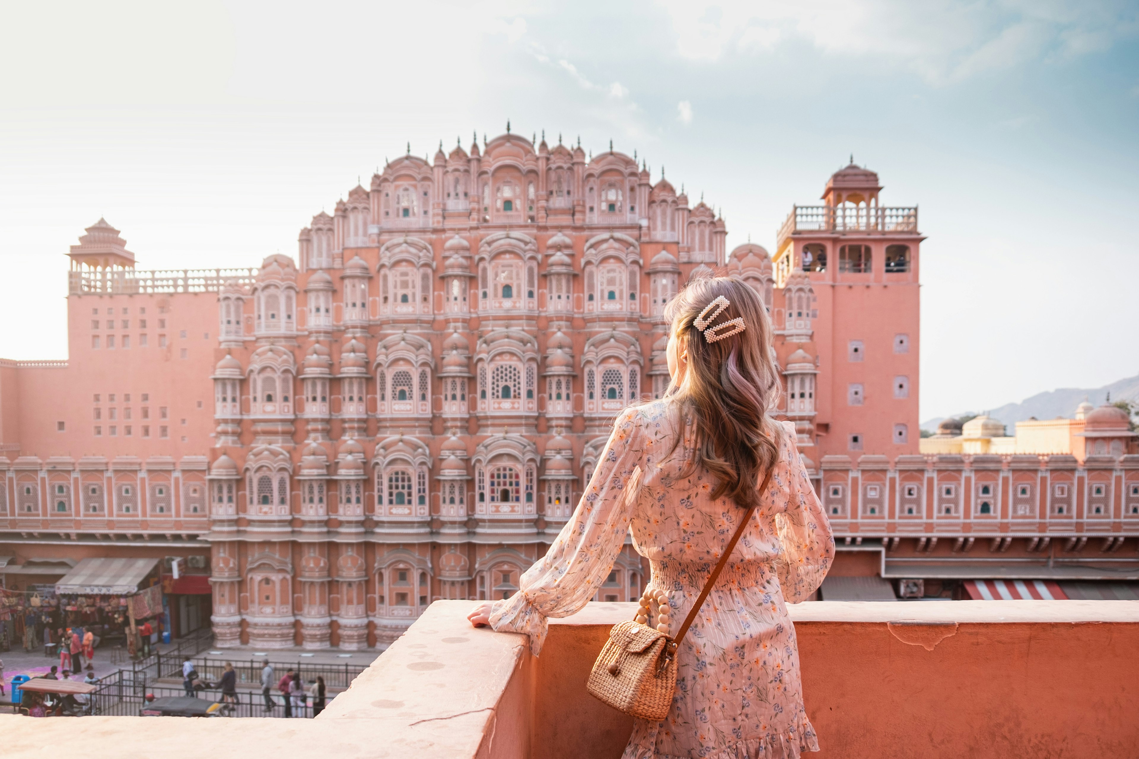 A female figure stands on a rooftop looking towards a huge pink building with hundreds of windows