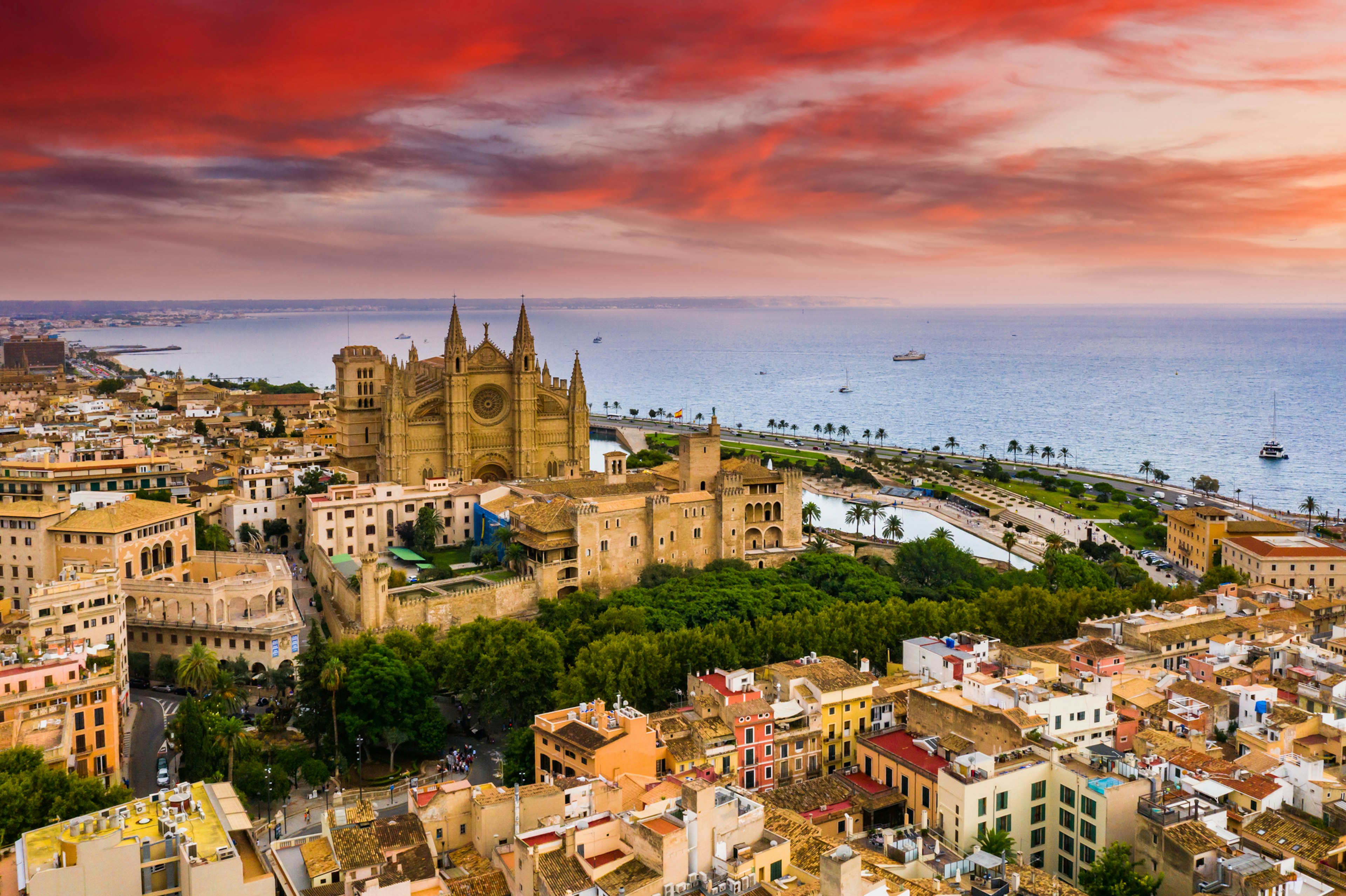 A large cathedral next to a boat-filled port as the sun sets