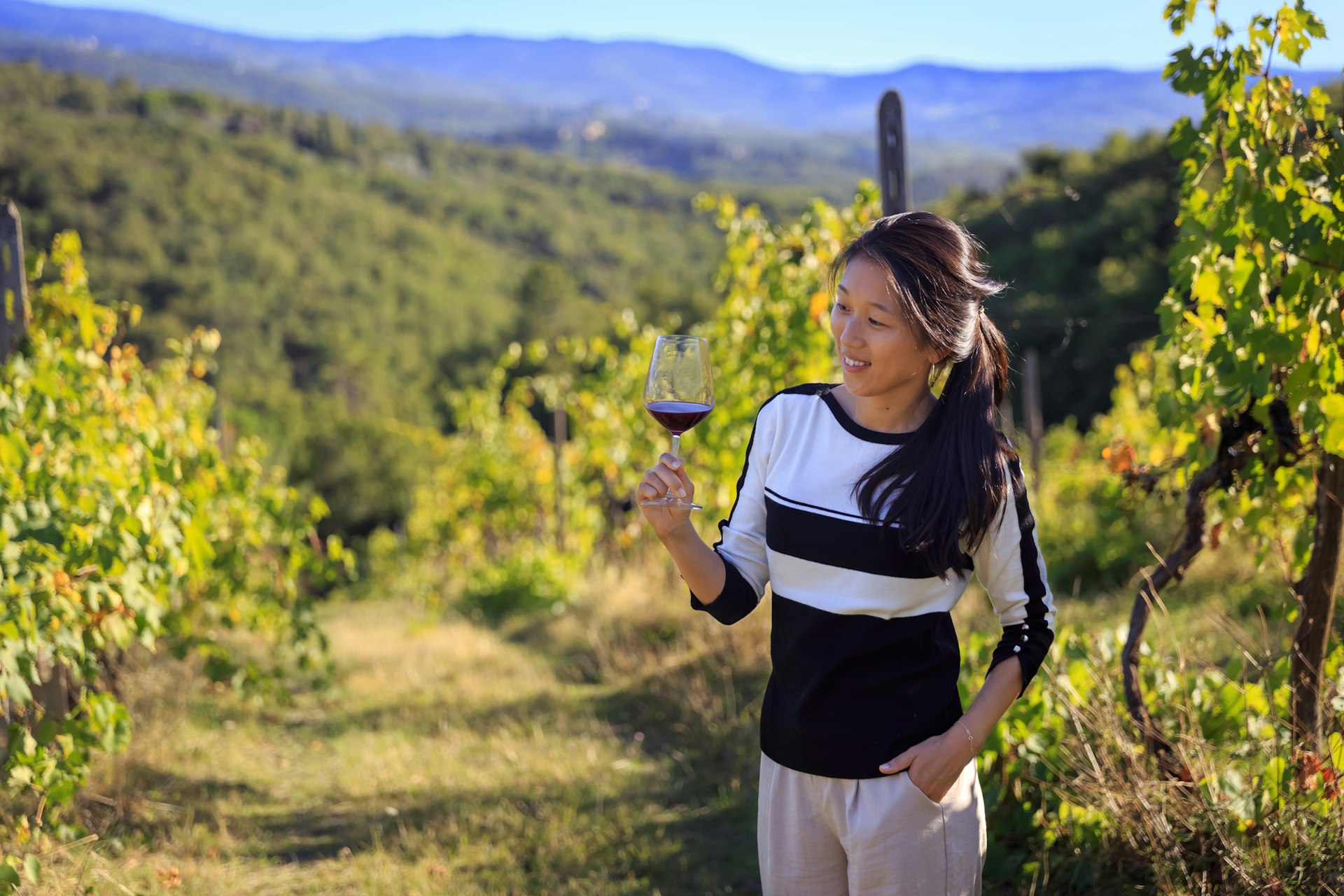 Young woman swirling wine around her glass while standing in vineyards 