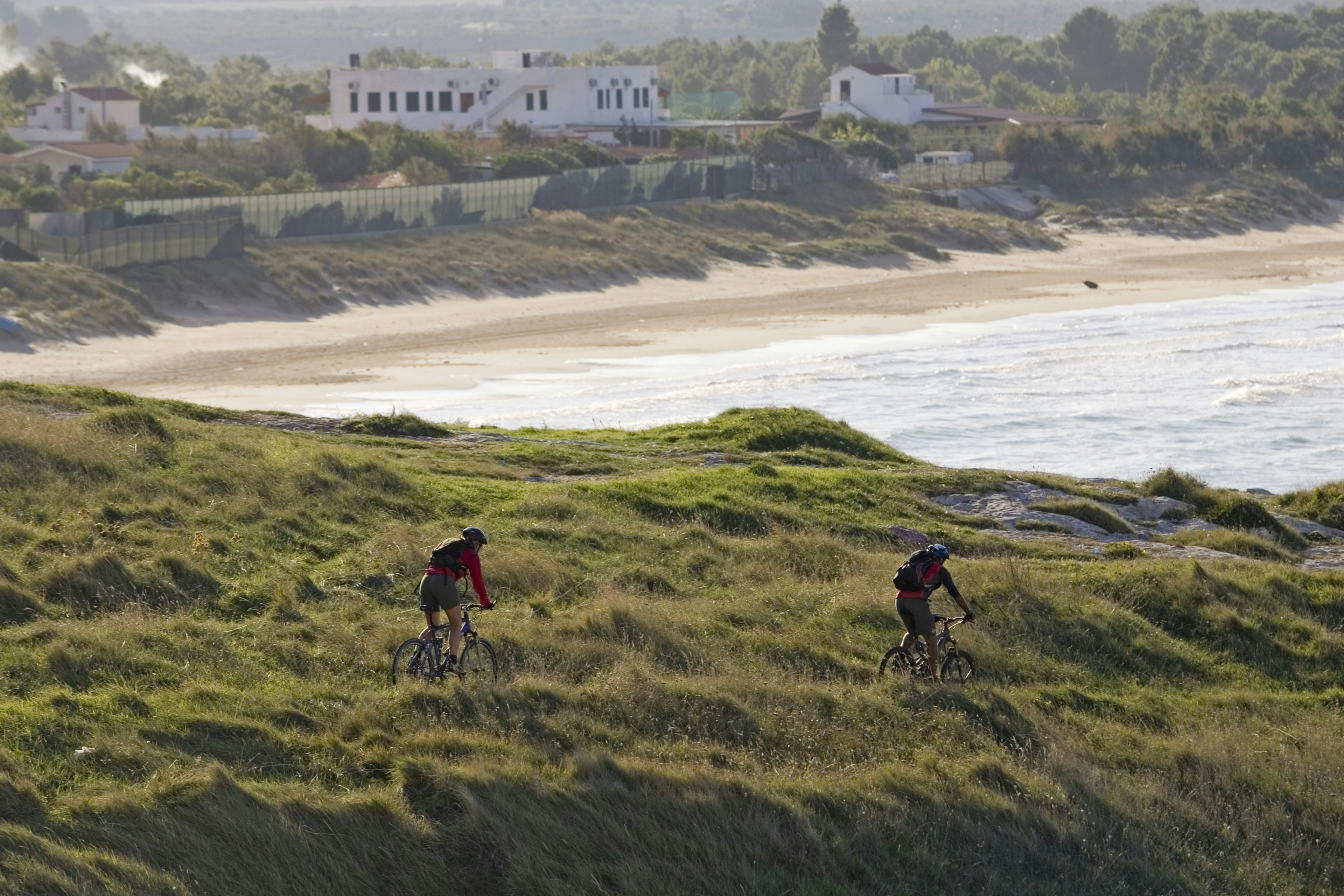 Two mountain-bike cyclists follow a trail on a bluff in Gargano, Puglia, Italy