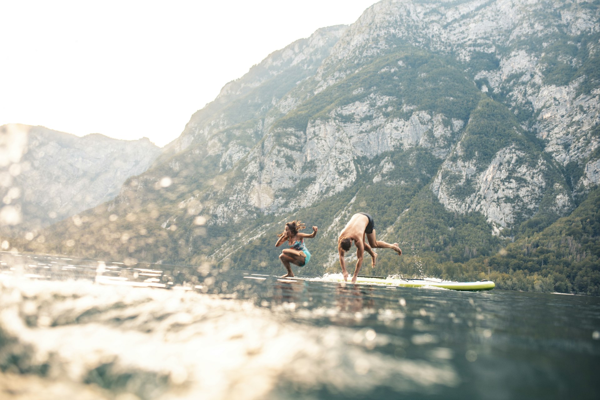 Two people jump off a paddleboard into a lake on a summer's day