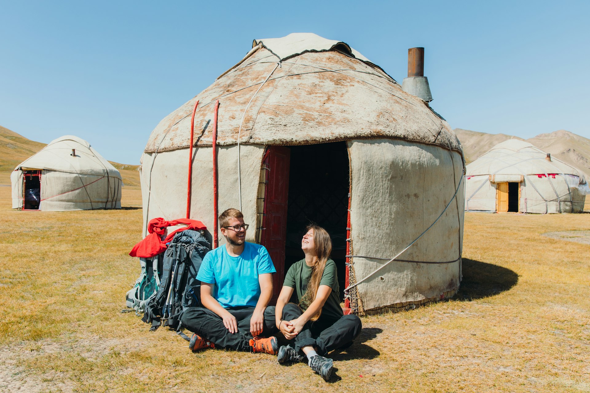 A man and a woman sit outside a yurt in the sunshine