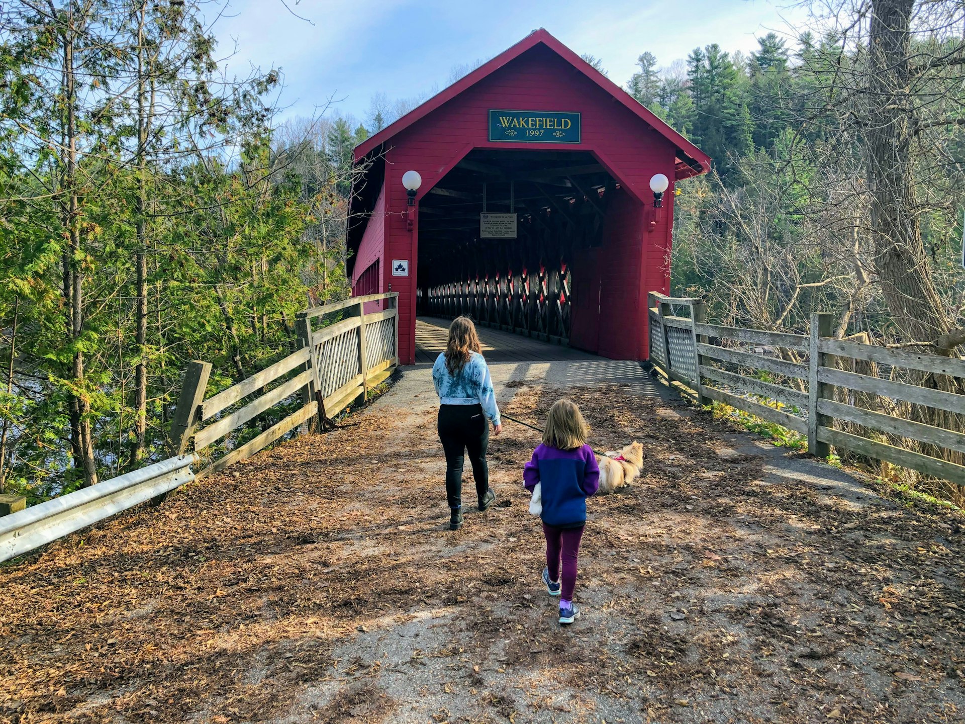 A mother and daughter approach the entrance of a wooden covered bridge painted red