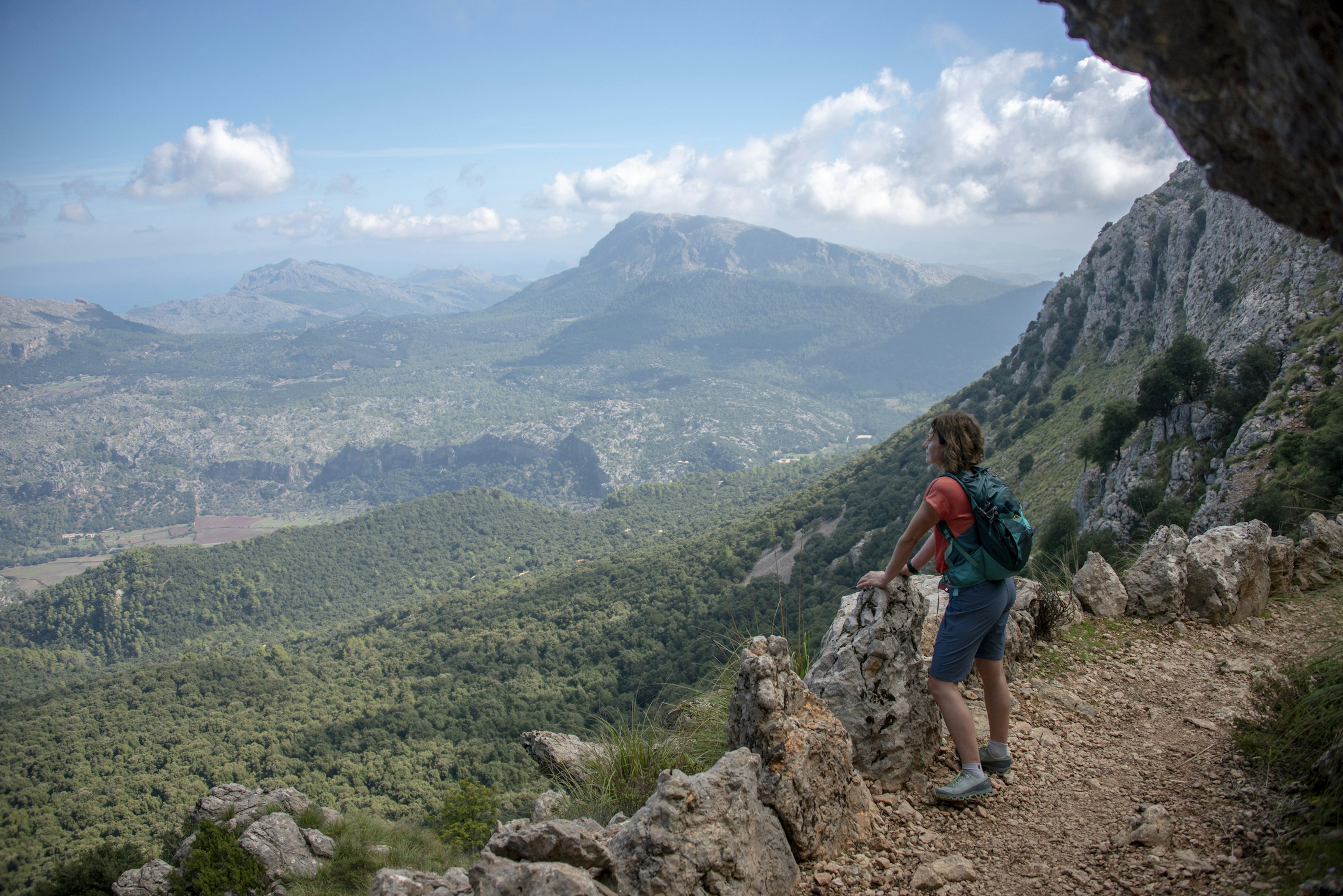 A hiker pauses on a trail to look out over the hilly landscape stretching out in front of her