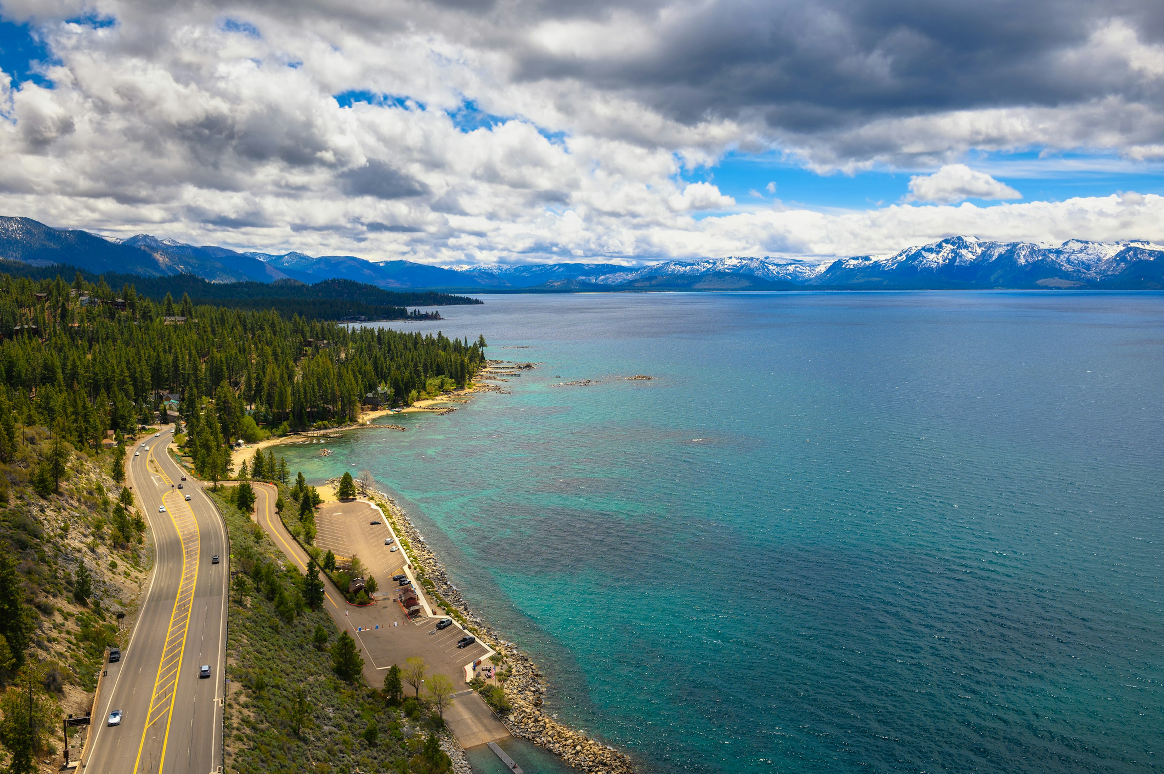 A road and car park next to a massive lake backed by a mountain range