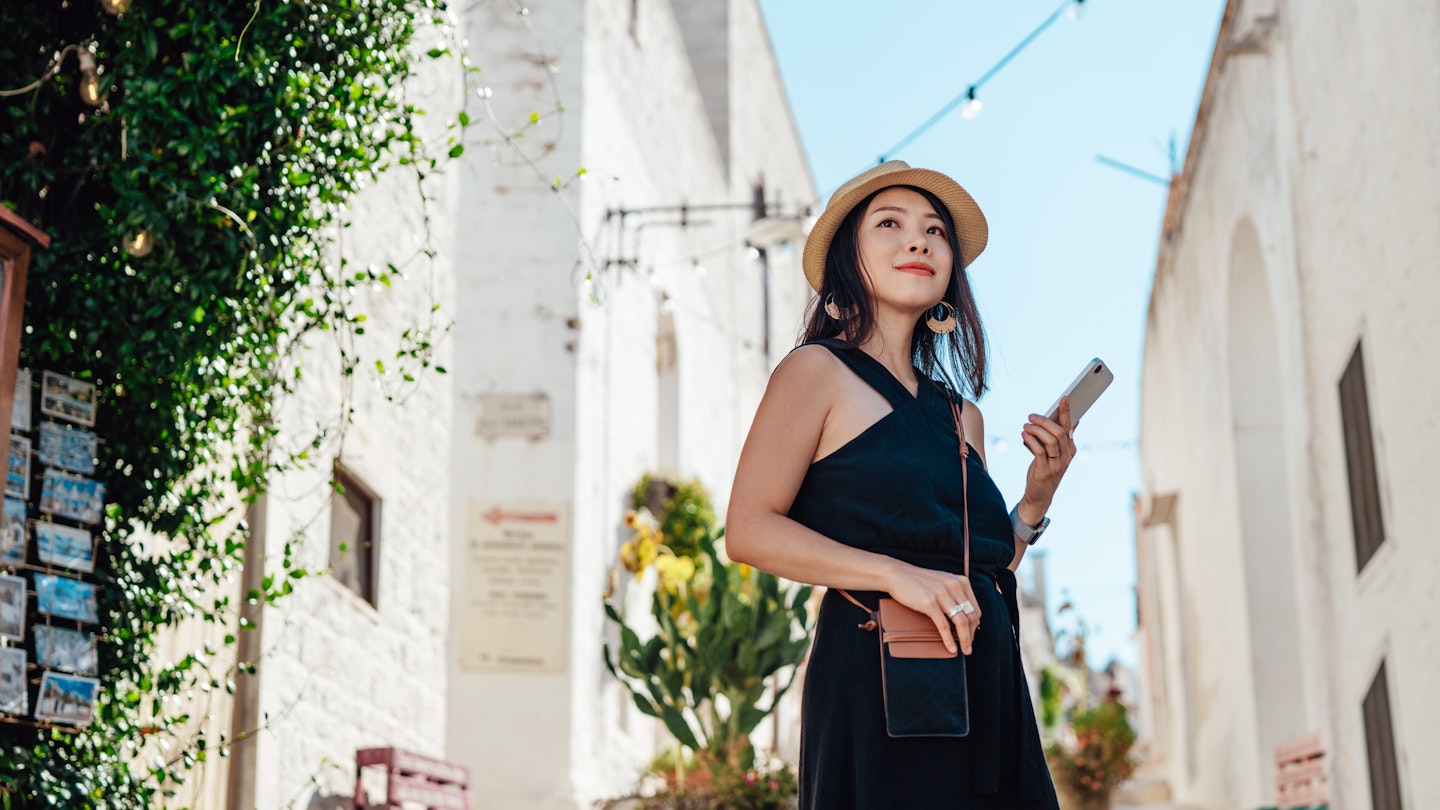 Low angle view of smiling young Asian woman with straw hat, using smart phone while walking in the old town, Puglia, Italy. Solo traveller. Technology and lifestyles.
1432971124