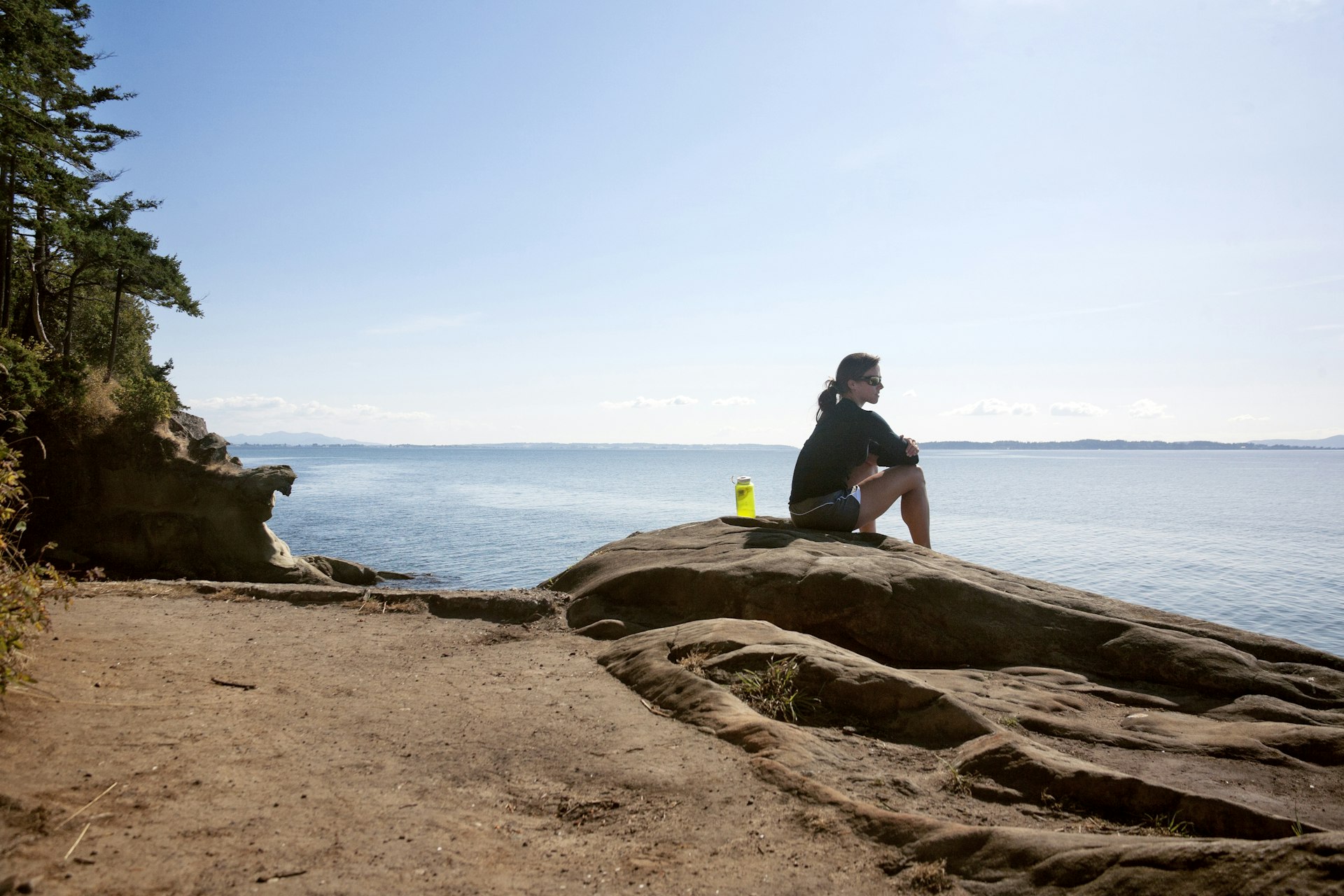 A woman sits on sandstone on the coastline of Larrabee State Park, Washington, USA