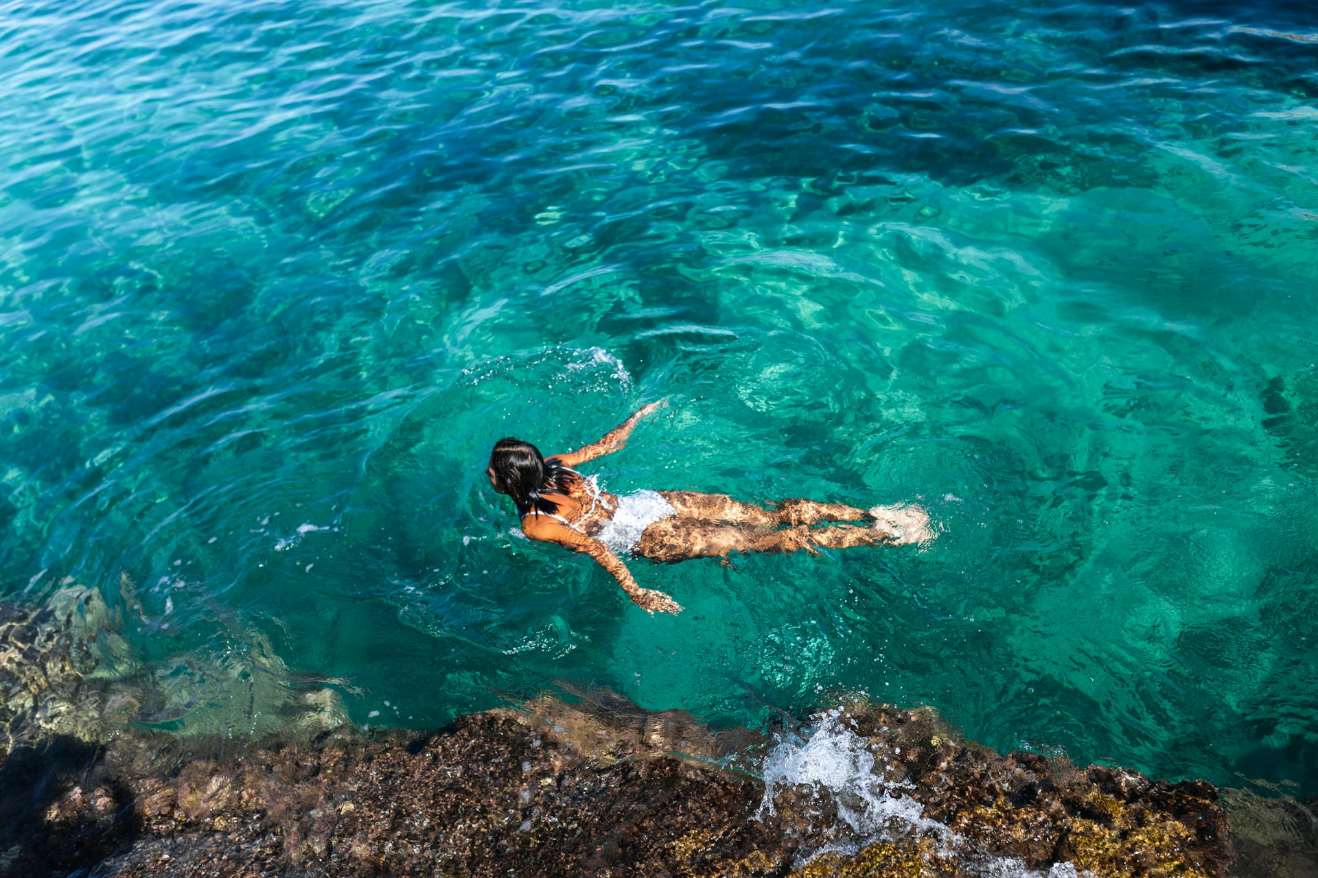Uma mulher de maiô branco nadando no mar da Sardenha