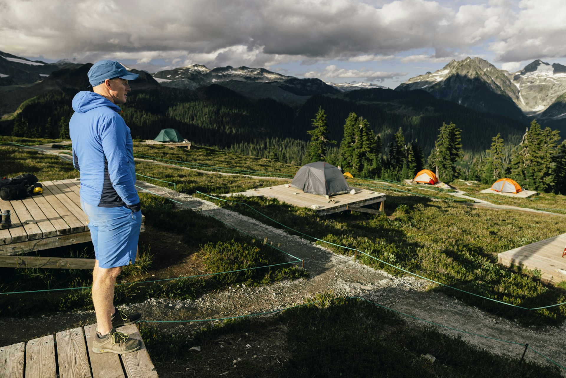 Um homem em um acampamento observa a dramática paisagem alpina perto do Lago Elfin, no Parque Provincial Garibaldi, Colúmbia Britânica, Canadá