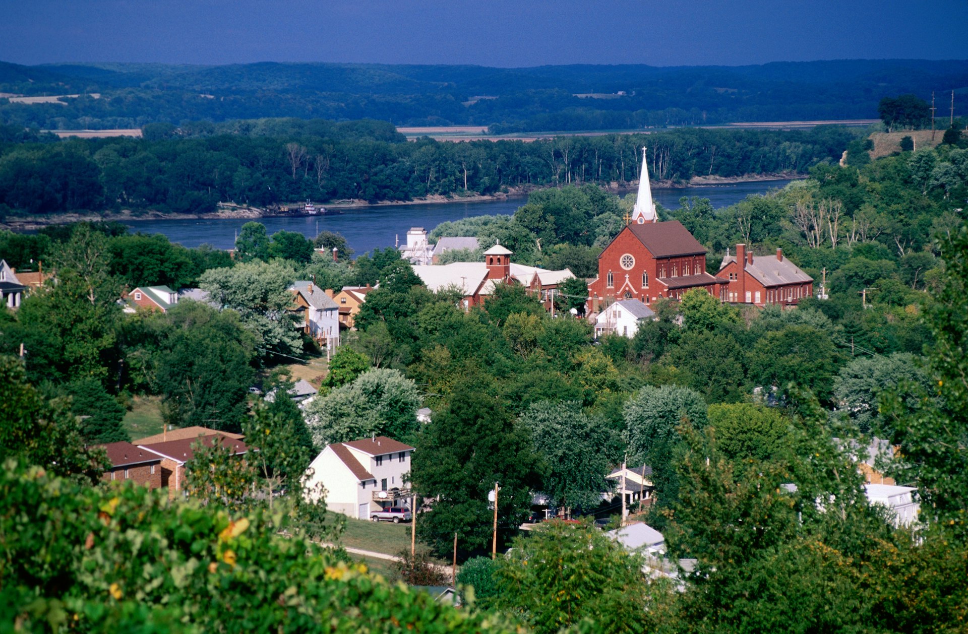 A town with a small red church with a pointed steeple next to a river