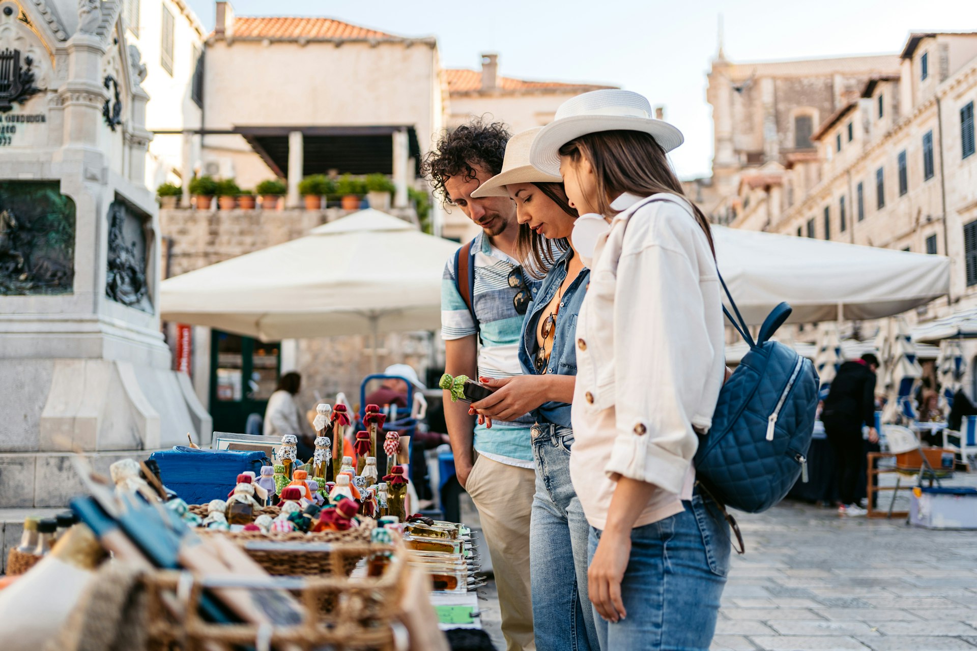 Three young tourists looking at the homemade liquors sold by the street vendors on the street in Dubrovnik in Croatia.