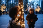 Mom playing peek-a-boo with her baby boy in New York next to a decorated tree.