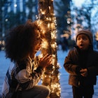 Mom playing peek-a-boo with her baby boy in New York next to a decorated tree.