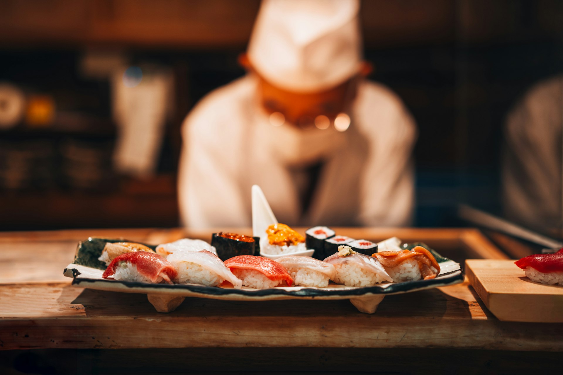 A plate of neat rice and fish sushi with the chef bowing in the background