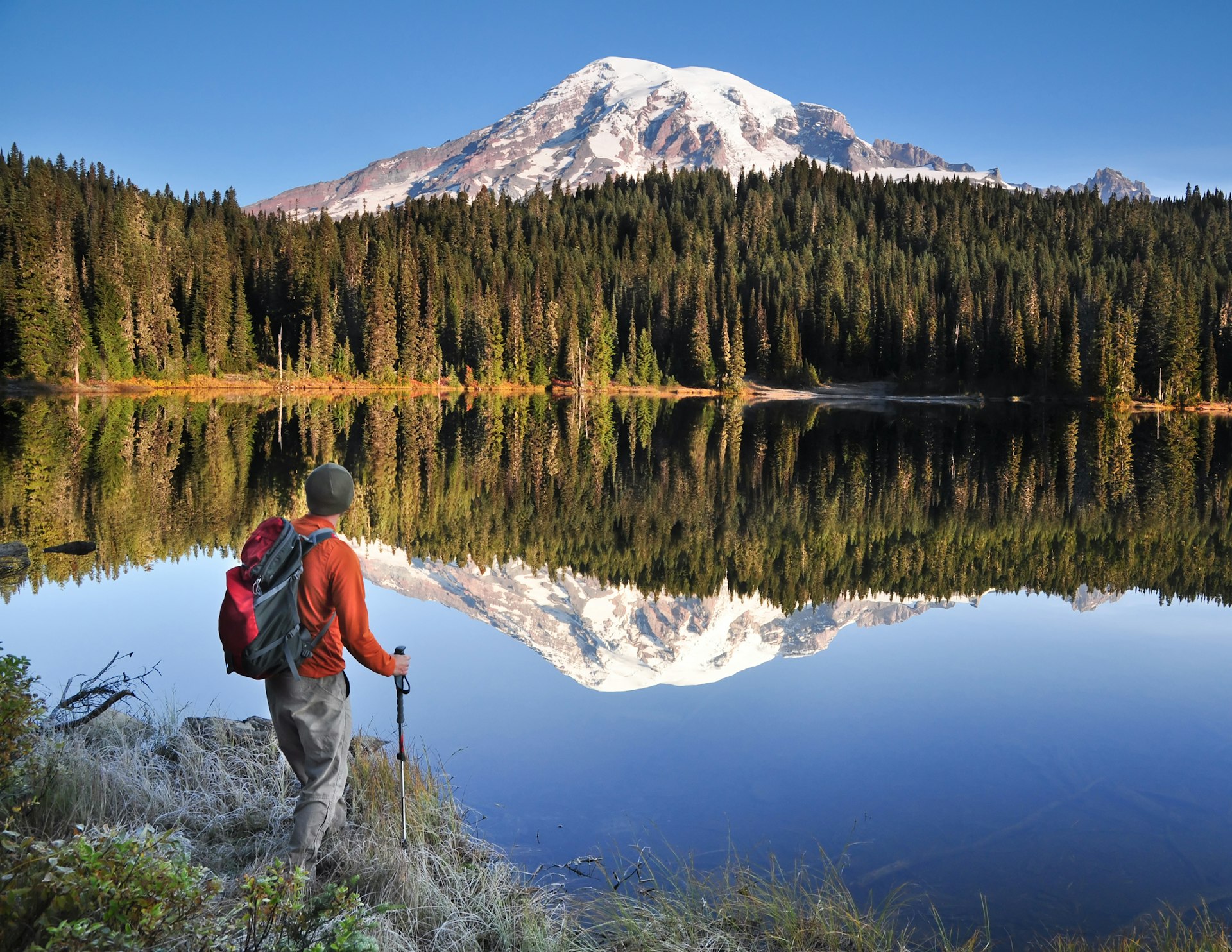 A hiker by a perfectly still Reflection Lake in Mt Rainier National Park, Washington State, USA