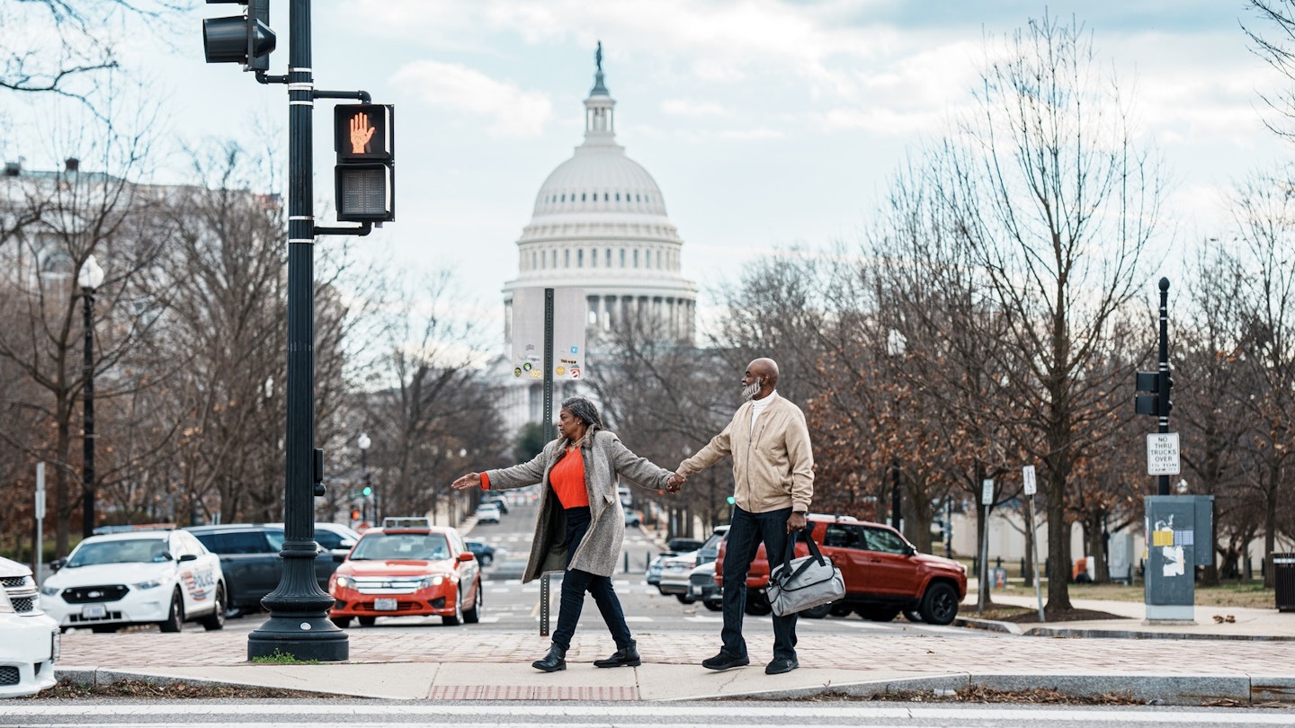A vibrant senior couple of African American Descent hold hands and wait at a crosswalk while exploring Washington DC on a winter vacation, with a view of the United States Capitol visible in the background..2052274115
2052274115
Adult,  Bag,  Car,  Female,  Handbag,  Pedestrian,  Person,  Shoe,  Traffic Light,  Vehicle,  Woman