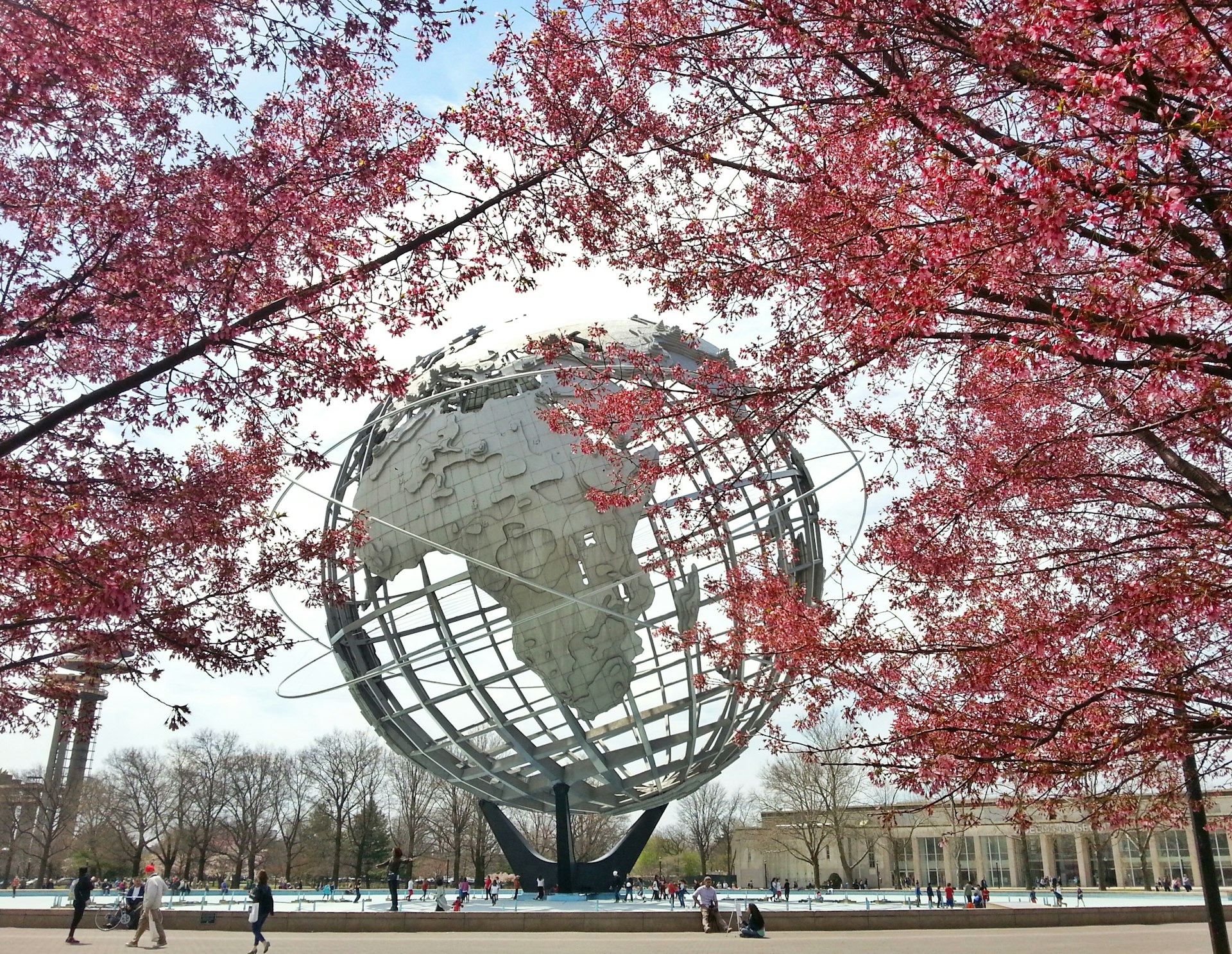 A large globe-like sculpture in the center of parkland surrounded by trees in blossom