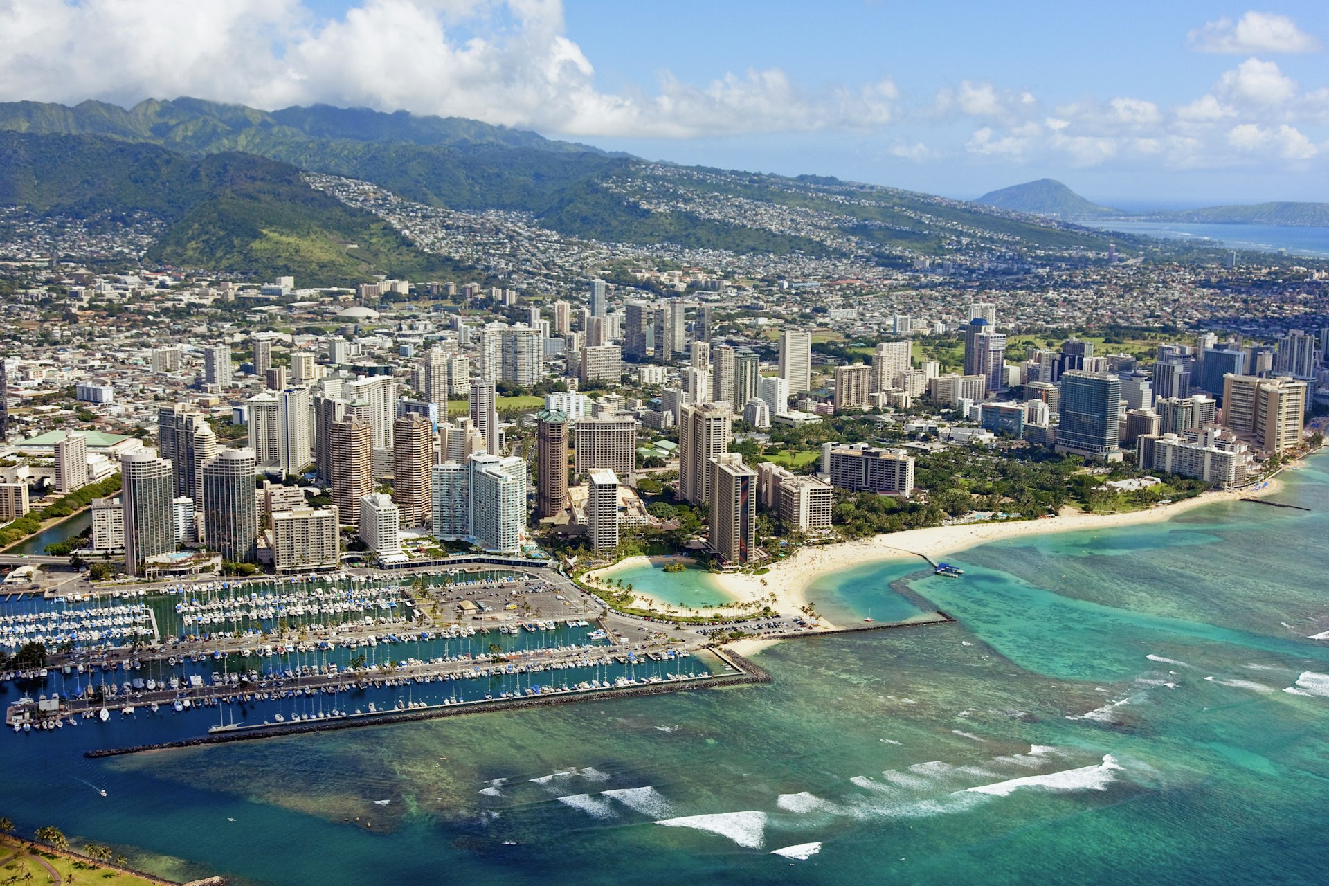 A large seaside city with tall buildings and greenery-covered volcanic hills rising behind
