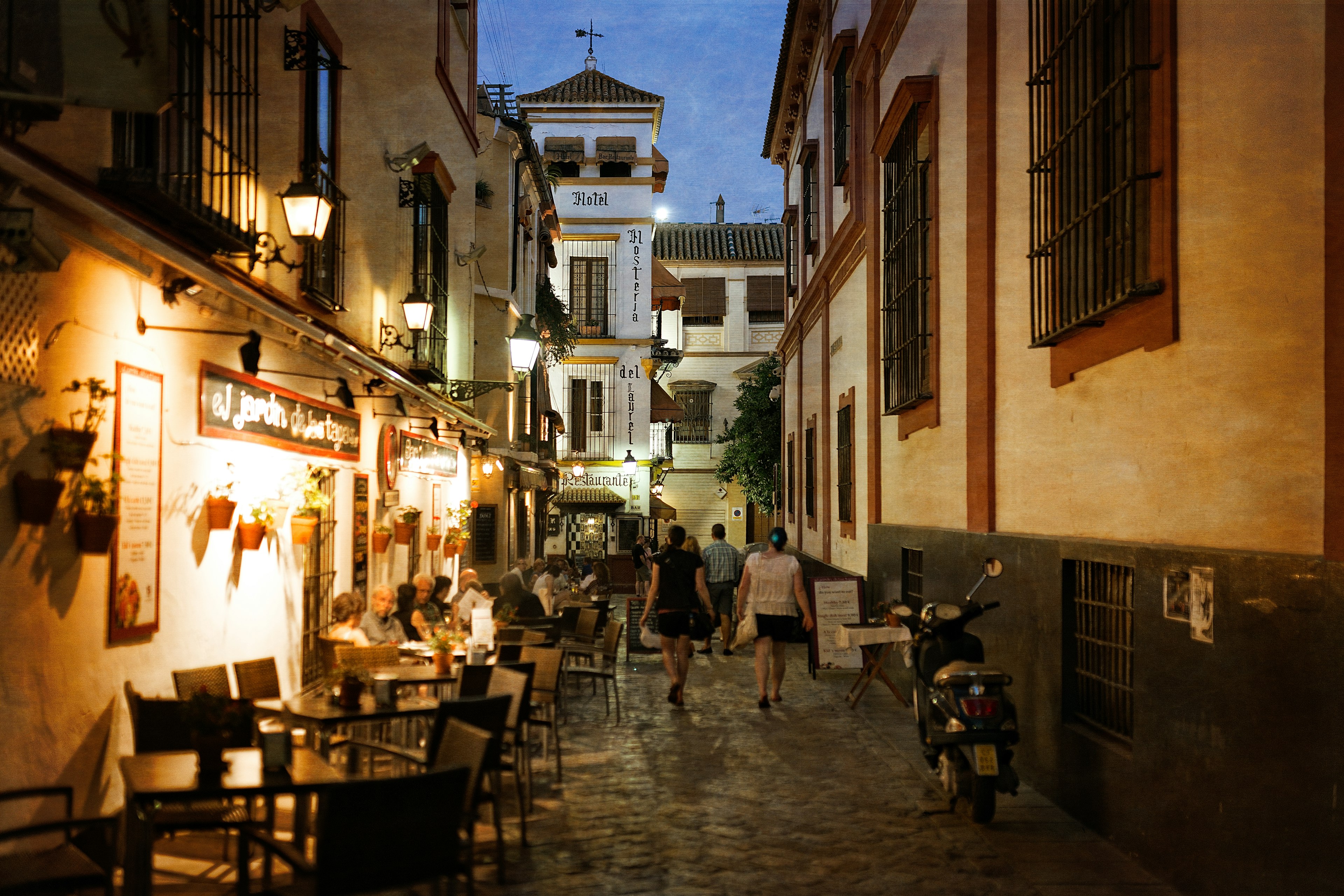 People sit outside at restaurant tables tucked down a side street