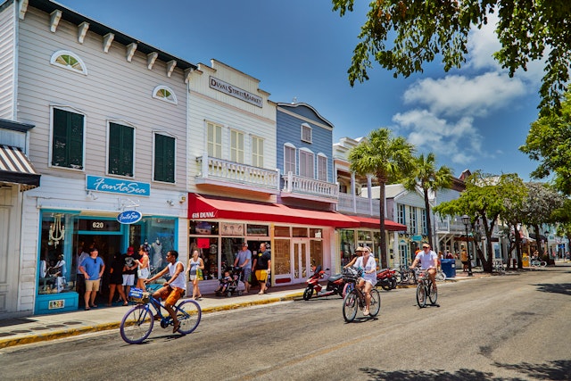 Cyclists riding past the colorful shopfronts on Duval Street in Key West