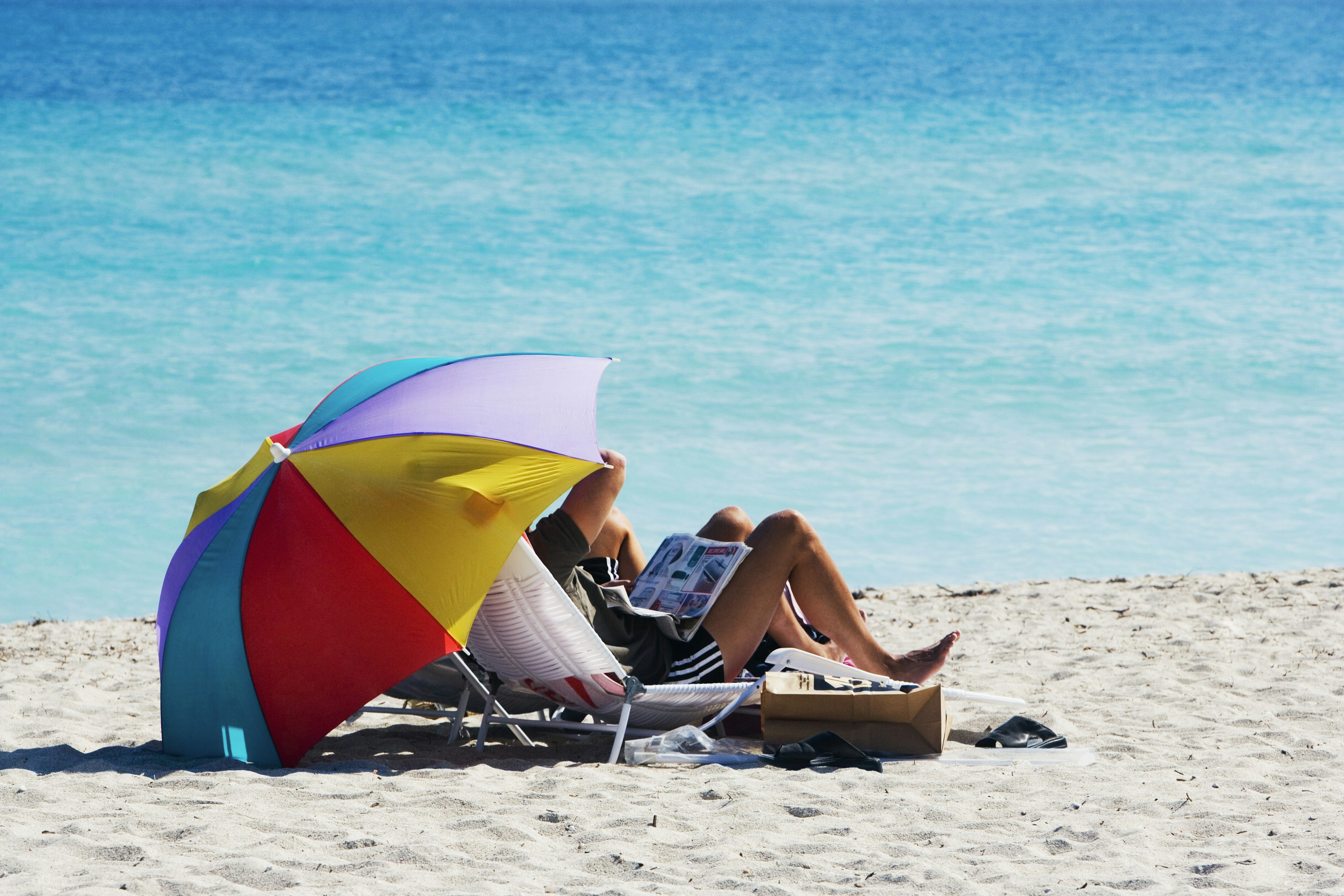 Two people under a rainbow beach umbrella, Miami, Florida, USA