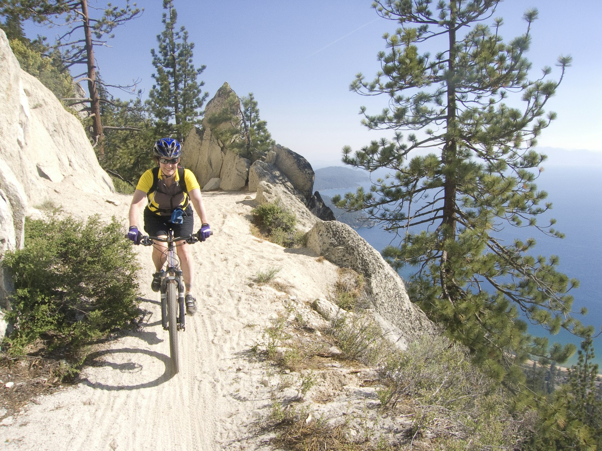 Uma mulher em uma mountain bike sorri enquanto desce uma trilha íngreme e arenosa