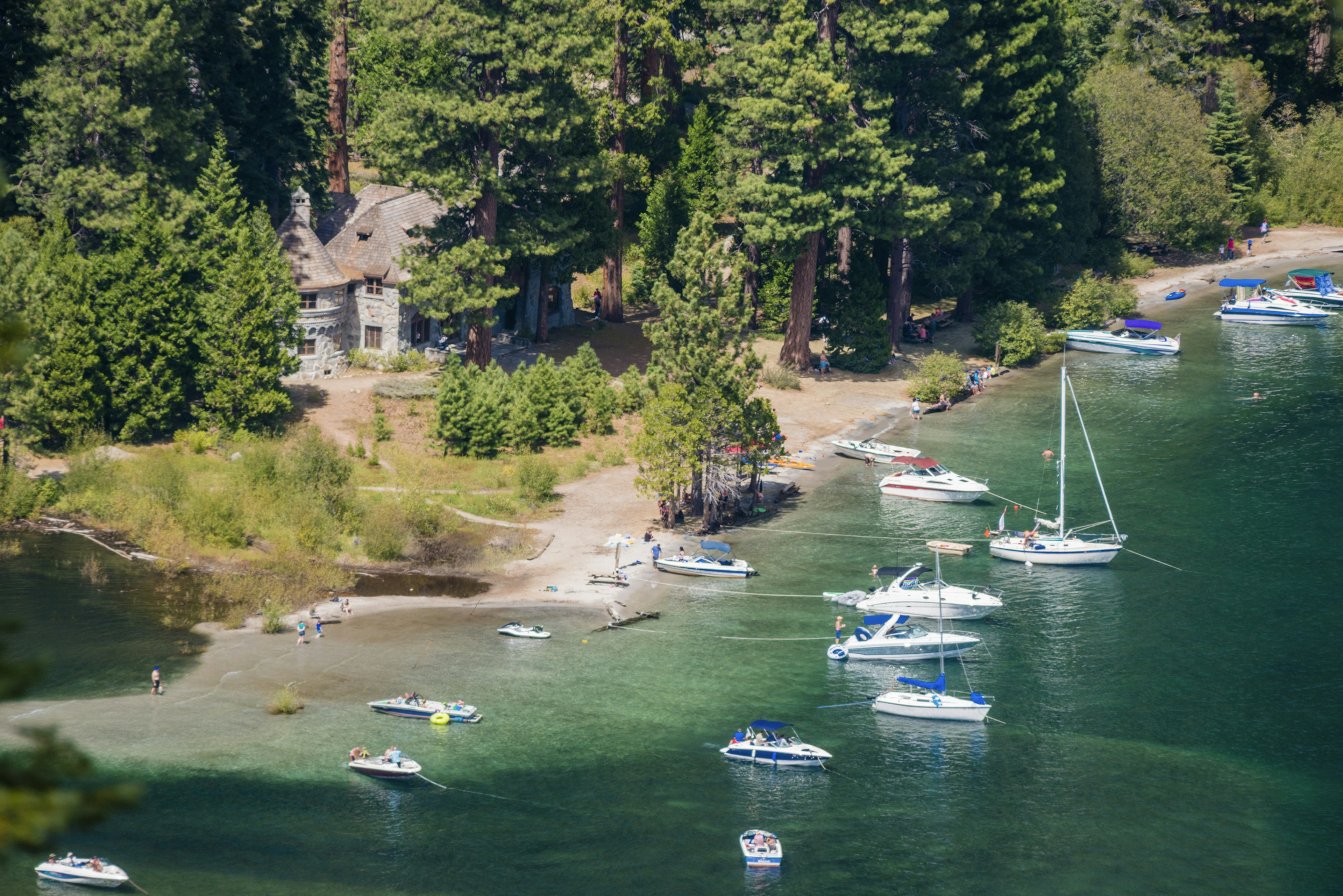 Small boats dock in a bay in front of a Scandinavian-style mansion surrounded by woodland