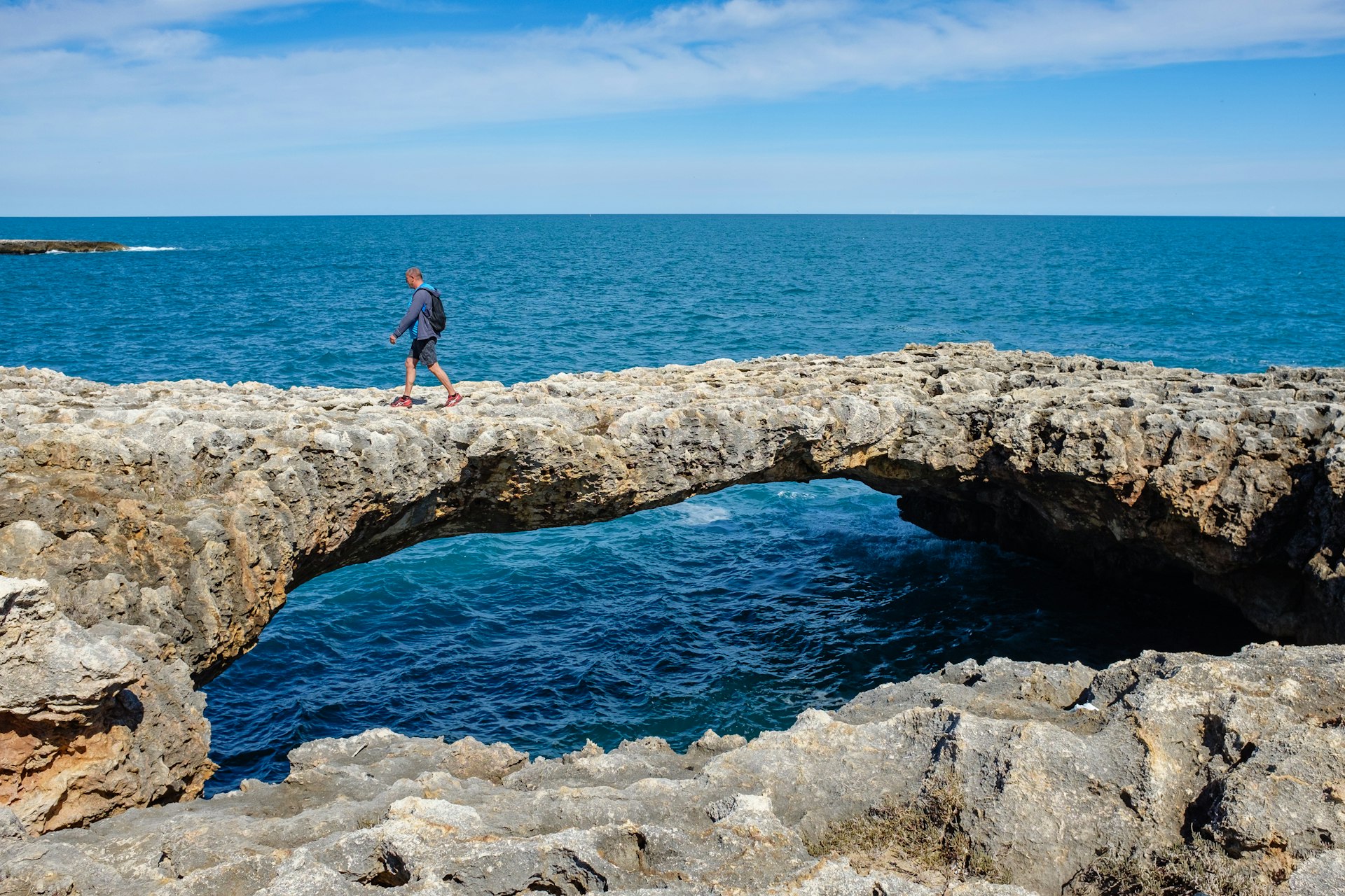 A man hikes on a natural rock bridge in Polignano a Mare, Puglia, Italy