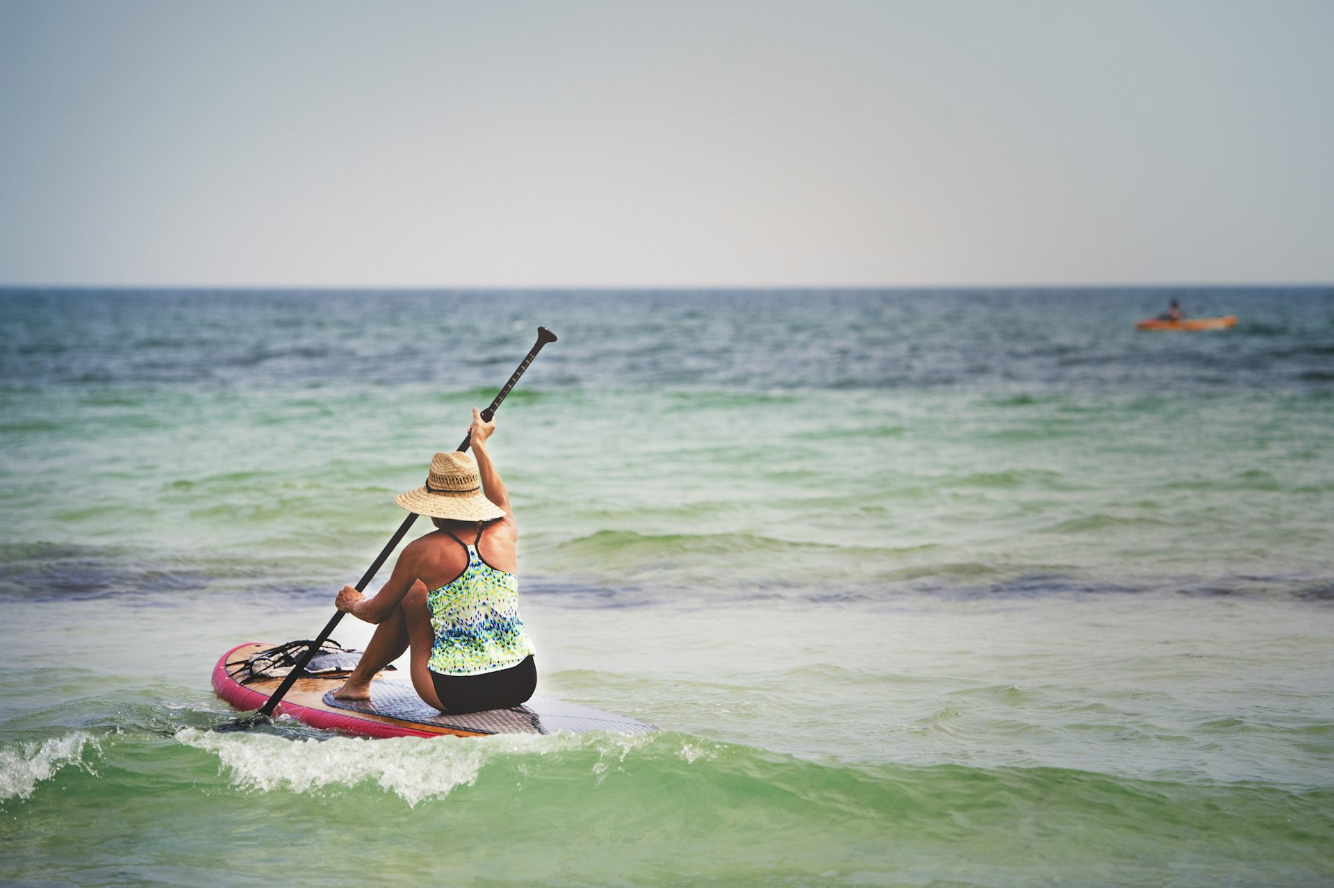 A senior woman paddles on a paddleboard in shallow water off the coastline of Pensacola, Florida