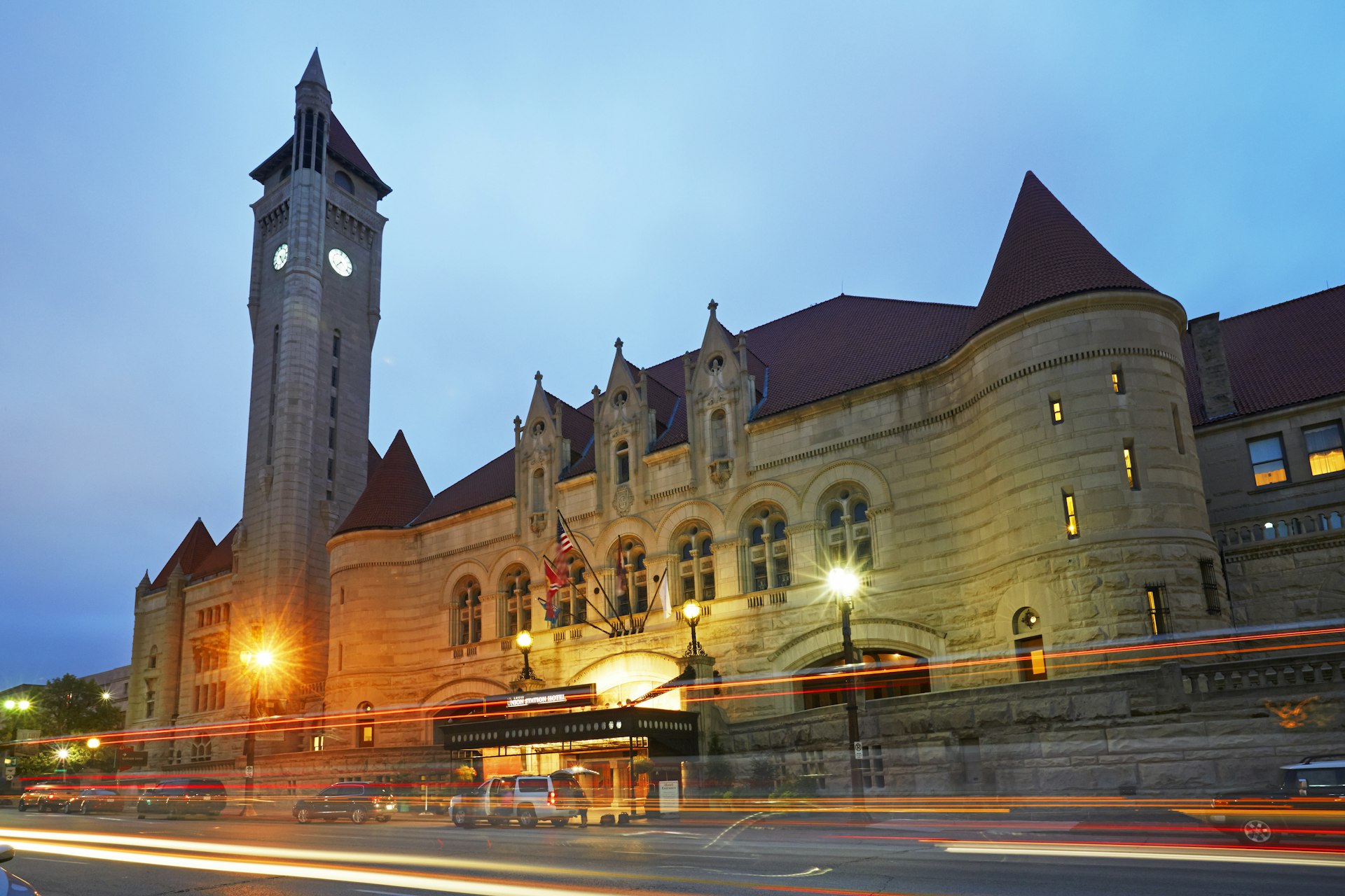 The facade of a grand station building at dusk as lights pass by