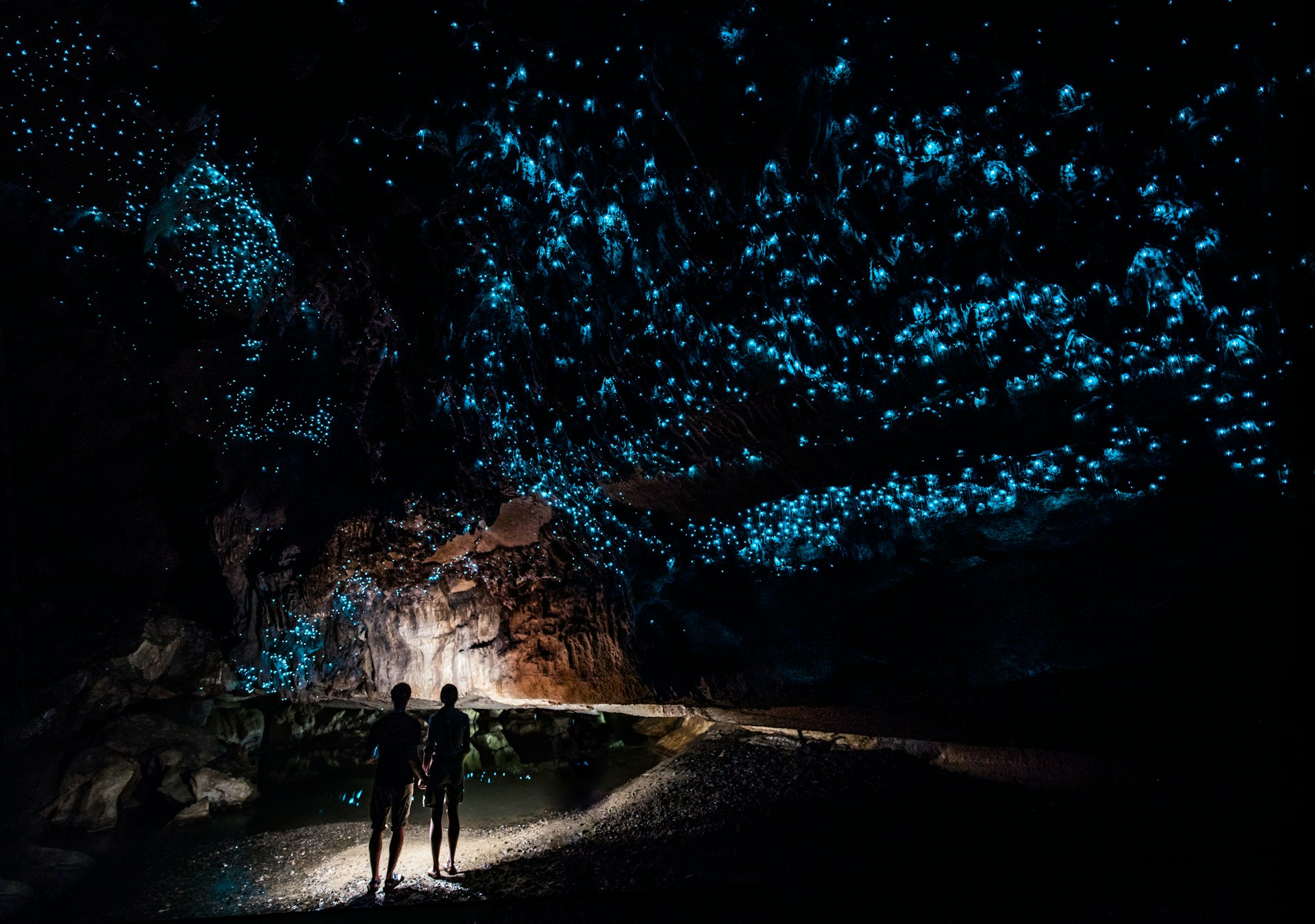 Two figures stand in a cave admiring the lights given off by glowworms