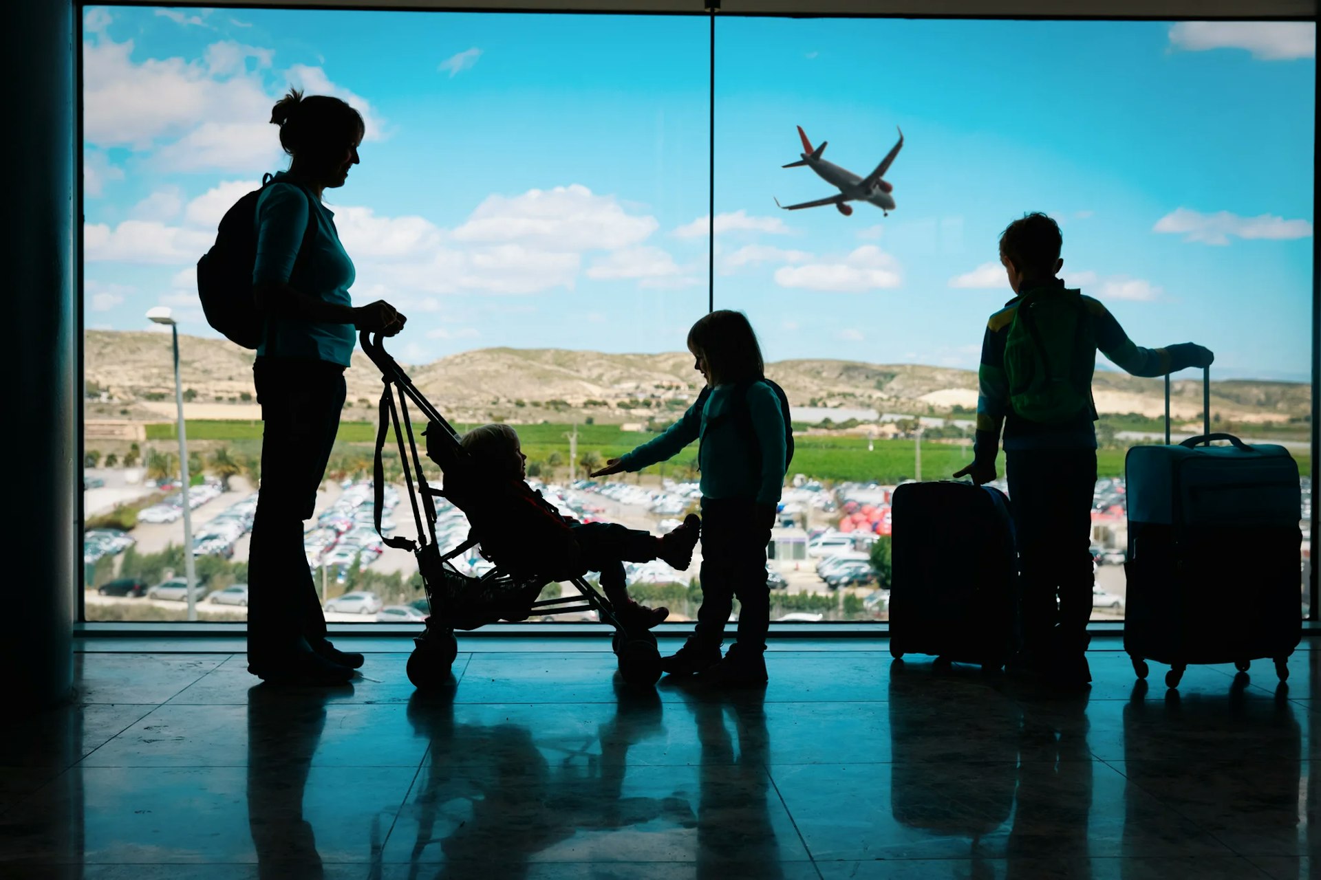 Silhouettes of a woman with a pram, a baby and two children with luggage at an airport 