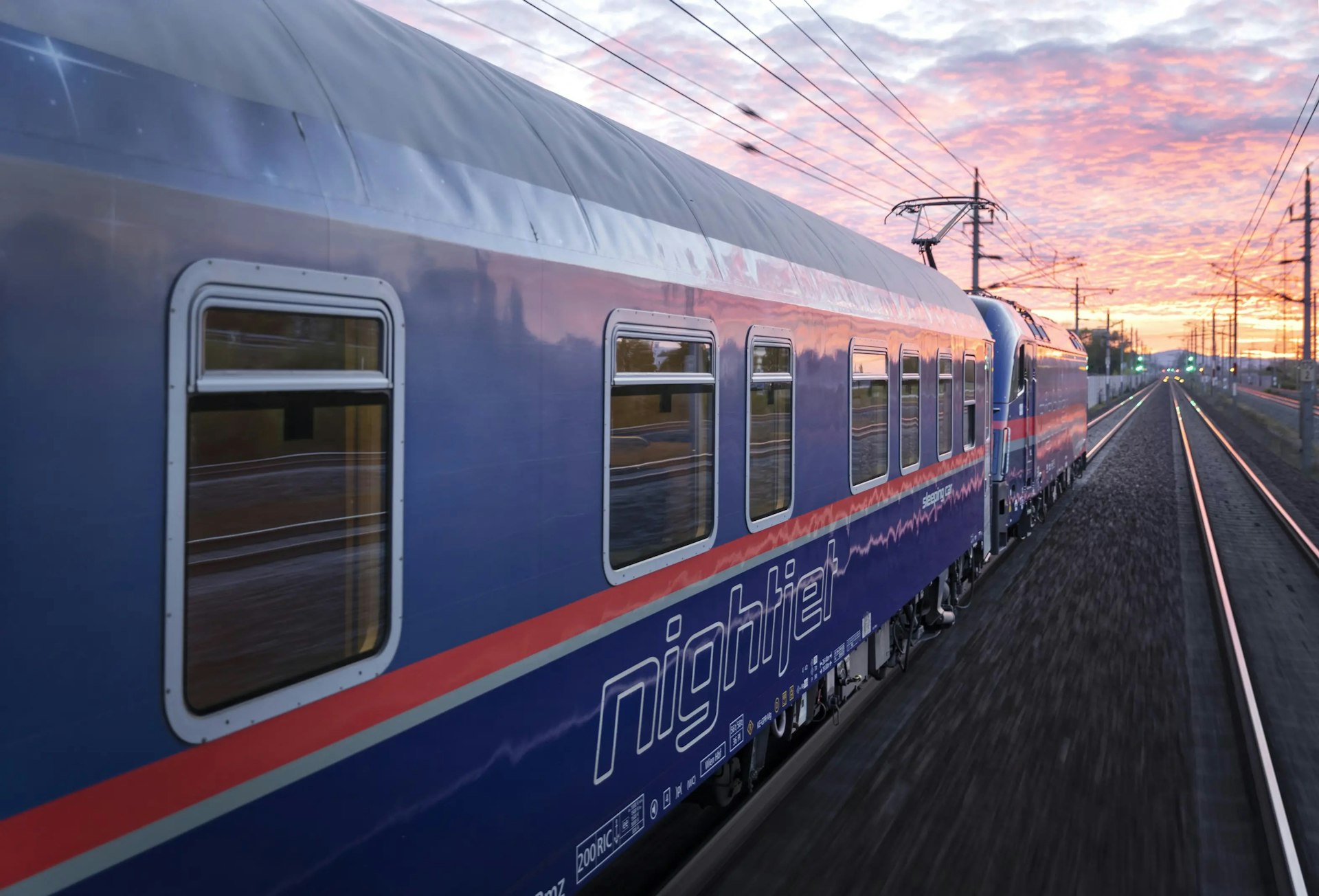 The exterior of a Nightjet train as the sun sets leaving pink and orange hues across the sky