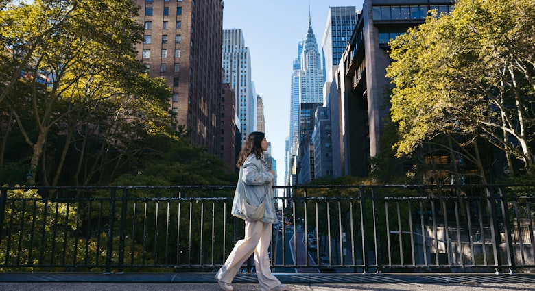 Side view of a young woman wearing an oversized denim jacket walking on the Tudor City Bridge, New York.