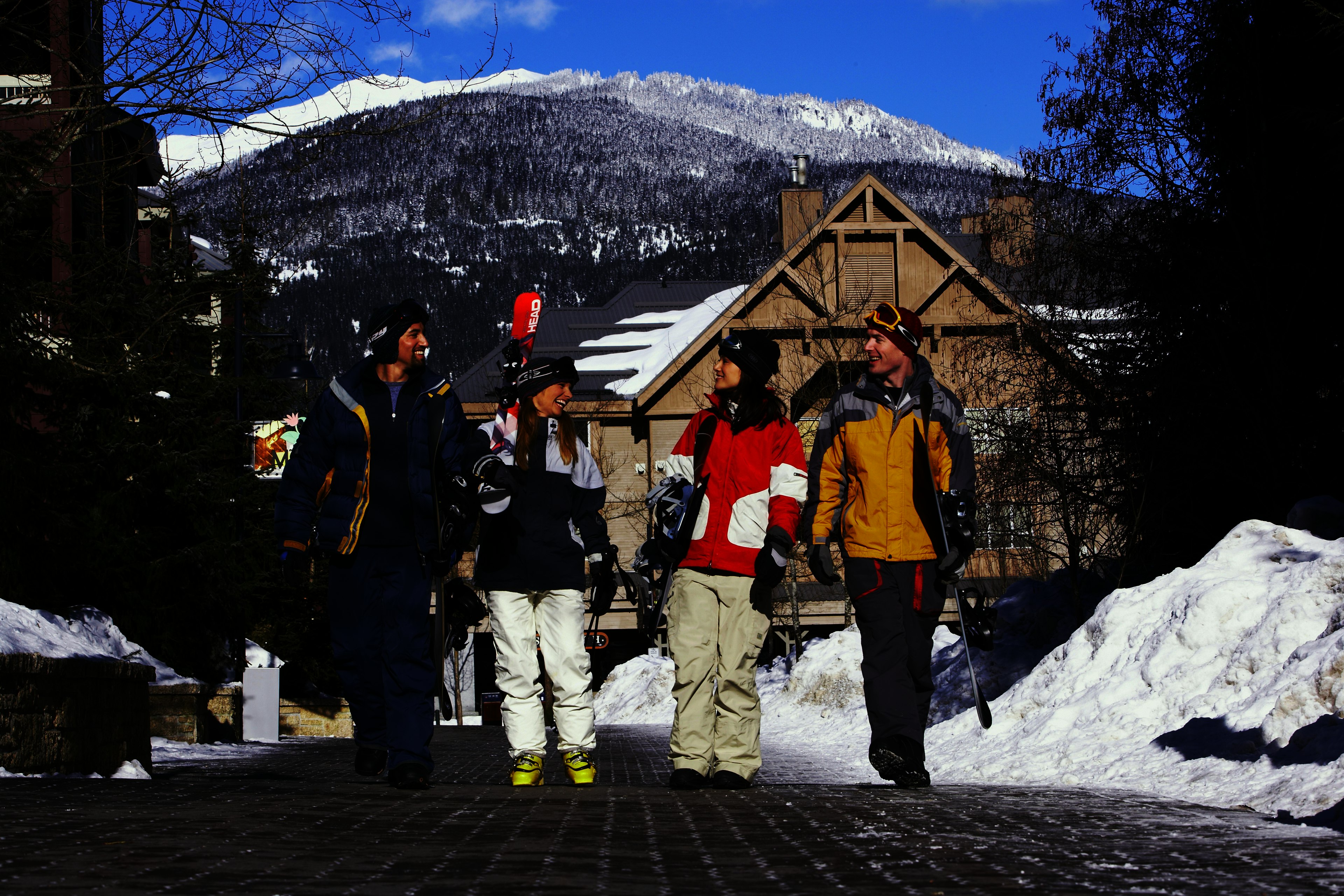 Adults walking along together chatting while carrying skis and snowboards