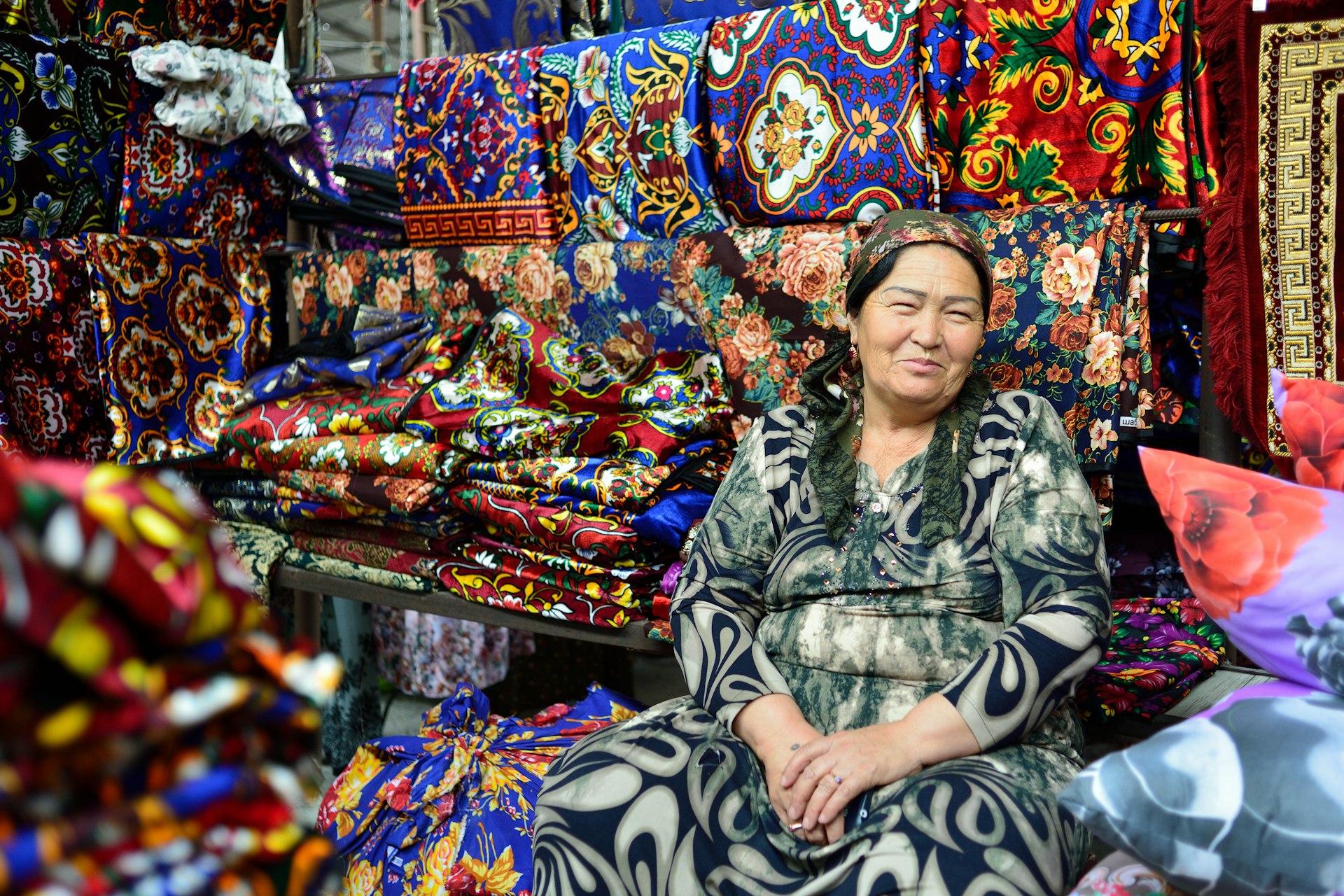 An Uzbek woman selling clothes in a market smiles at the camera