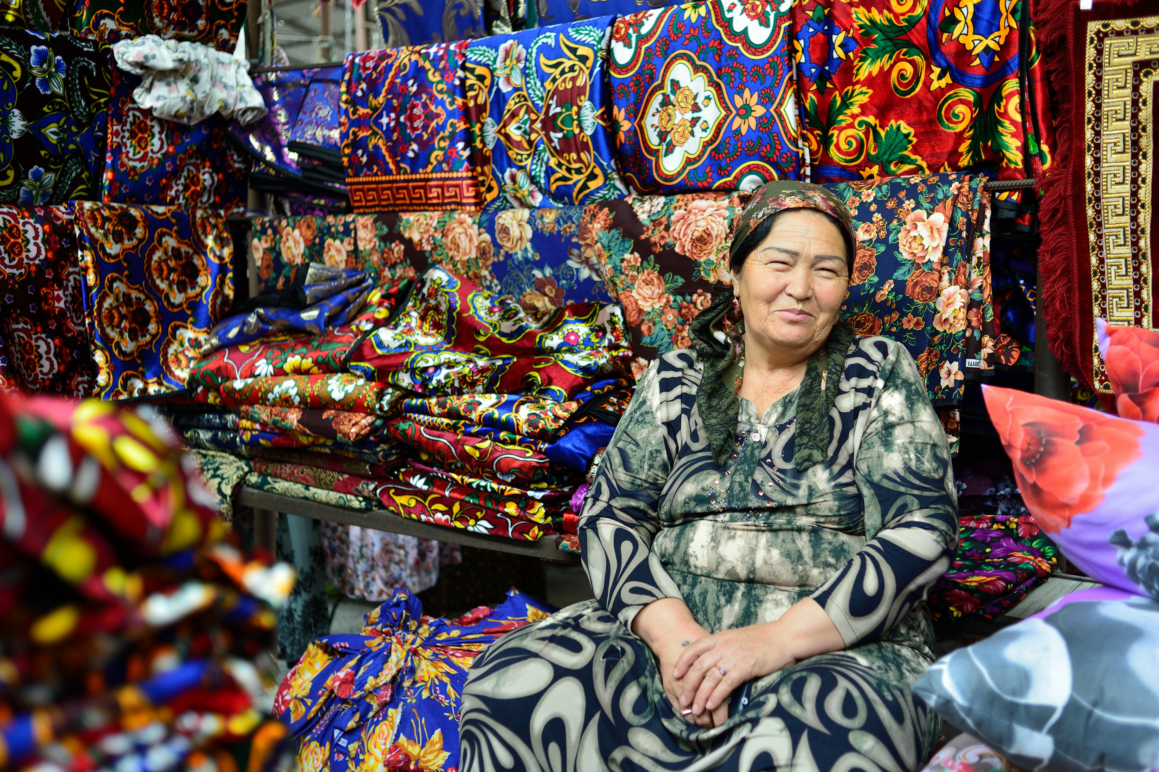 An Uzbek woman selling clothes in a market smiles at the camera