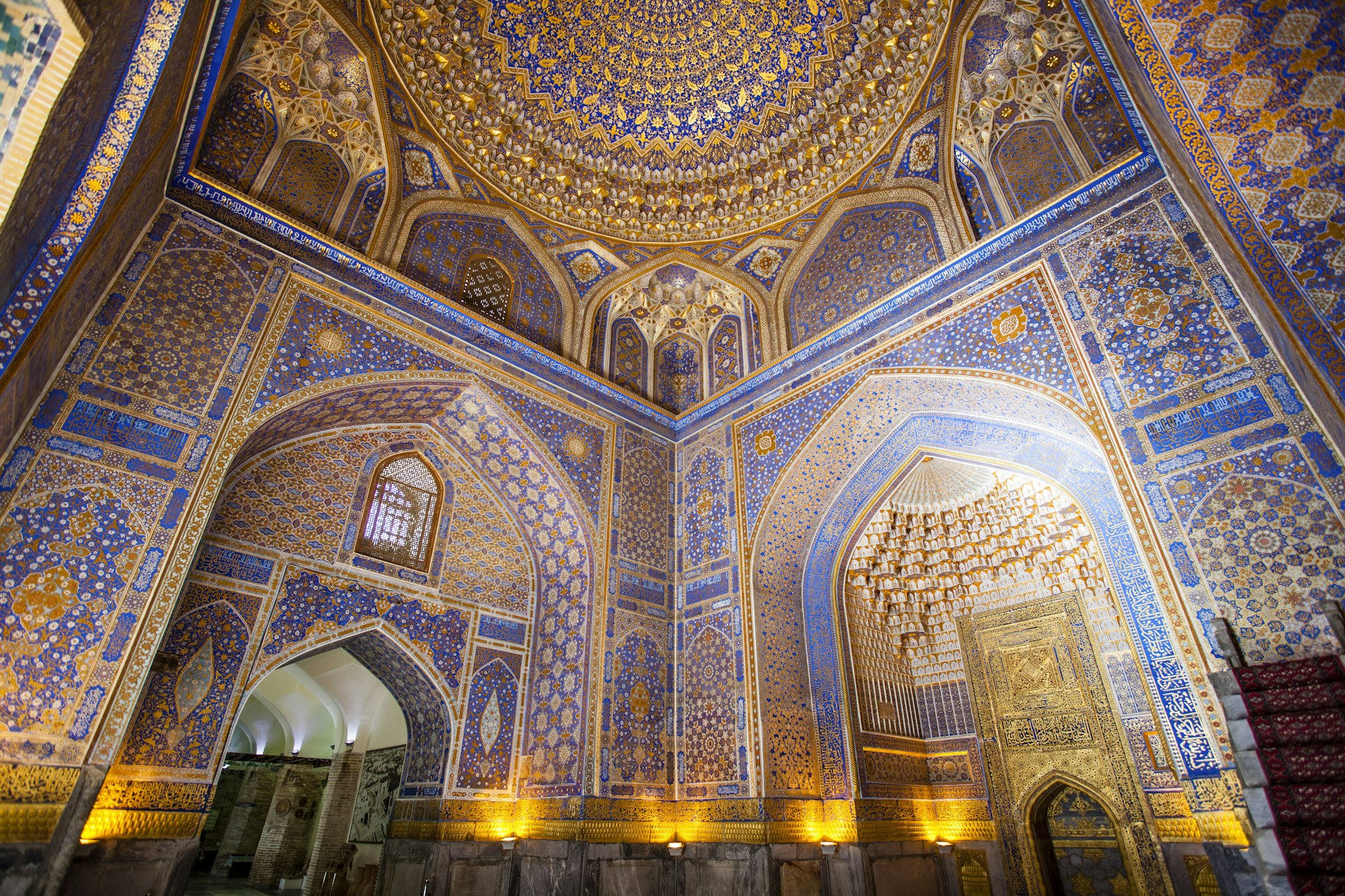 Intricately blue-and-gold tiled interior of a building with arched doorways and a central dome