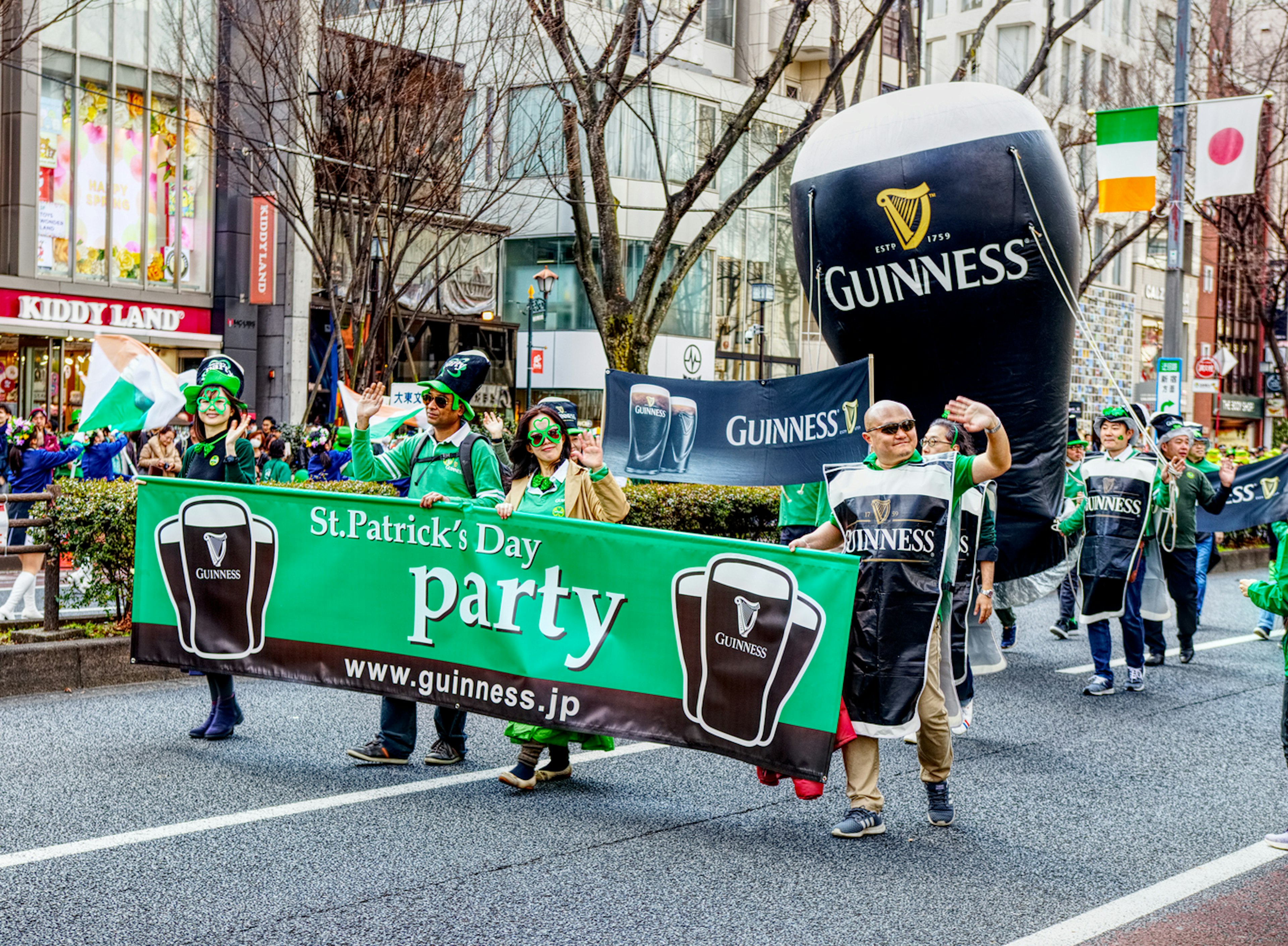 People parade along a street carrying a green banner and a large inflatable pint of Guinness, a black stout with a white top