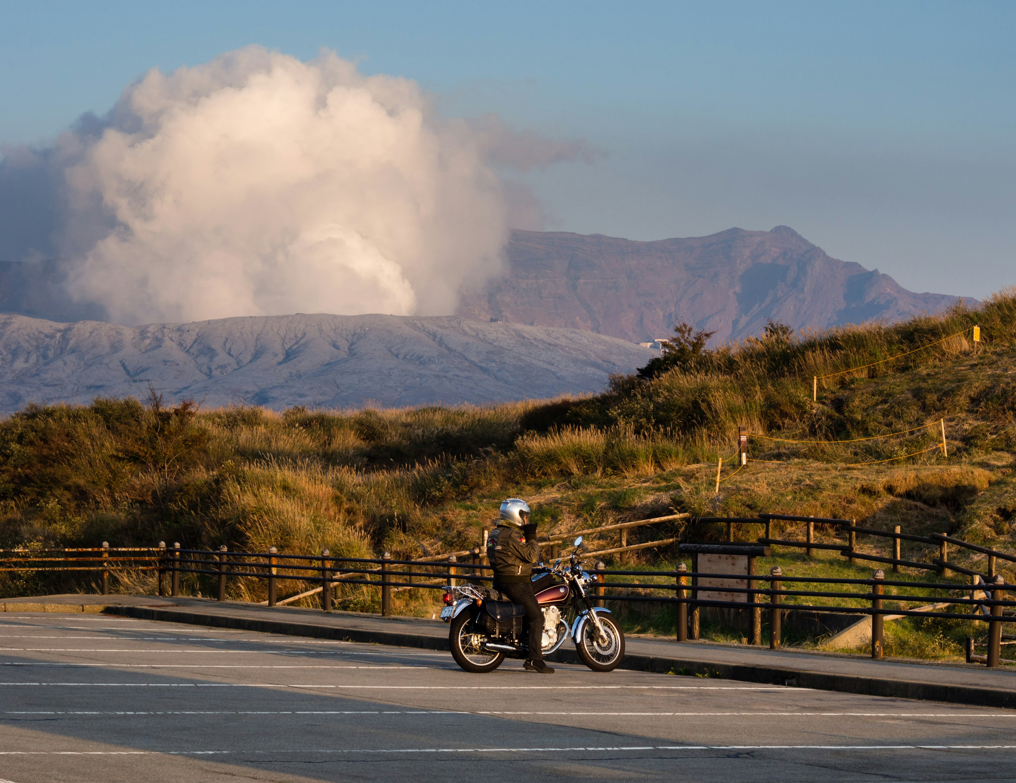 Biker stopped at Kusasenri parking lot with fuming Nakadake crater at the background, Aso, Japan