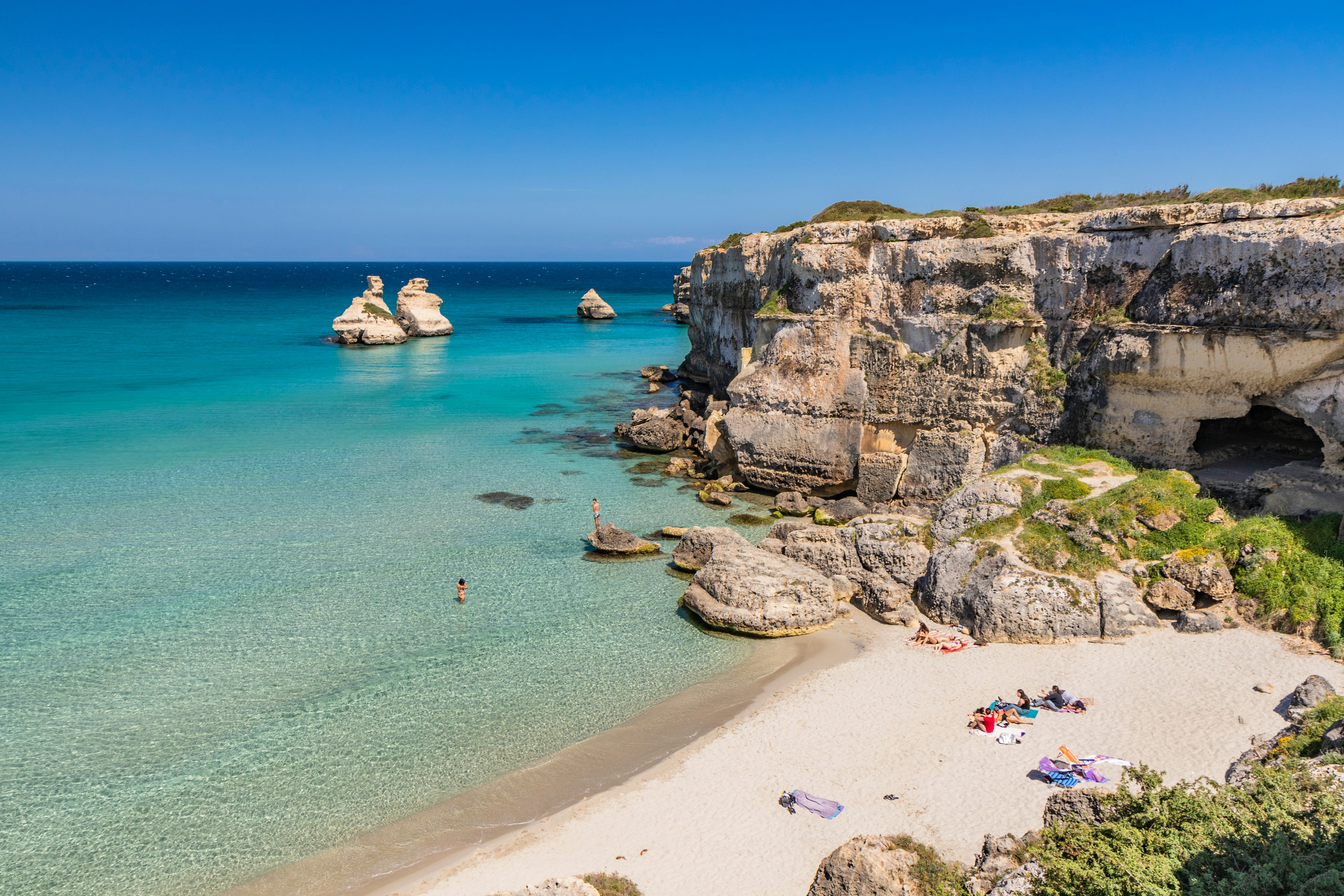 A small beach tucked in at the base of a cliff with a family relaxing in the sun